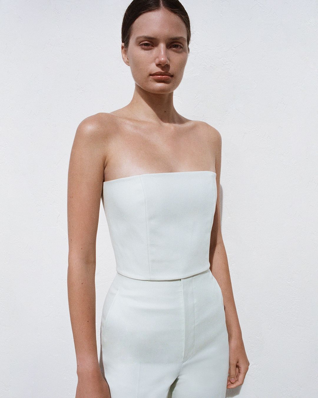 Girl looking at the camera with shadow across her face, wearing green strapless top and trousers.
