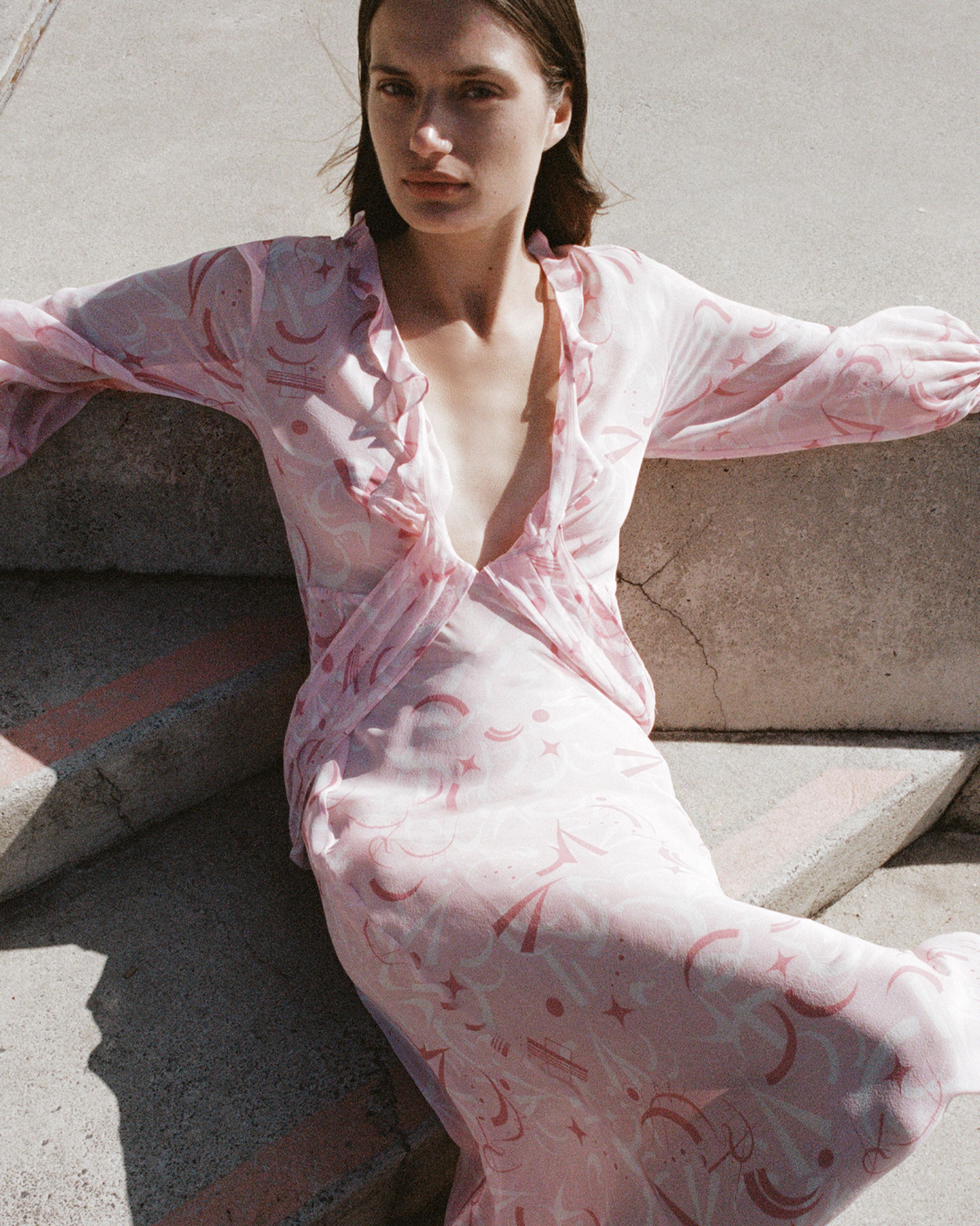 Girl looking at camera sitting on concrete stairs with arms stretched out the side and leg crossed. 