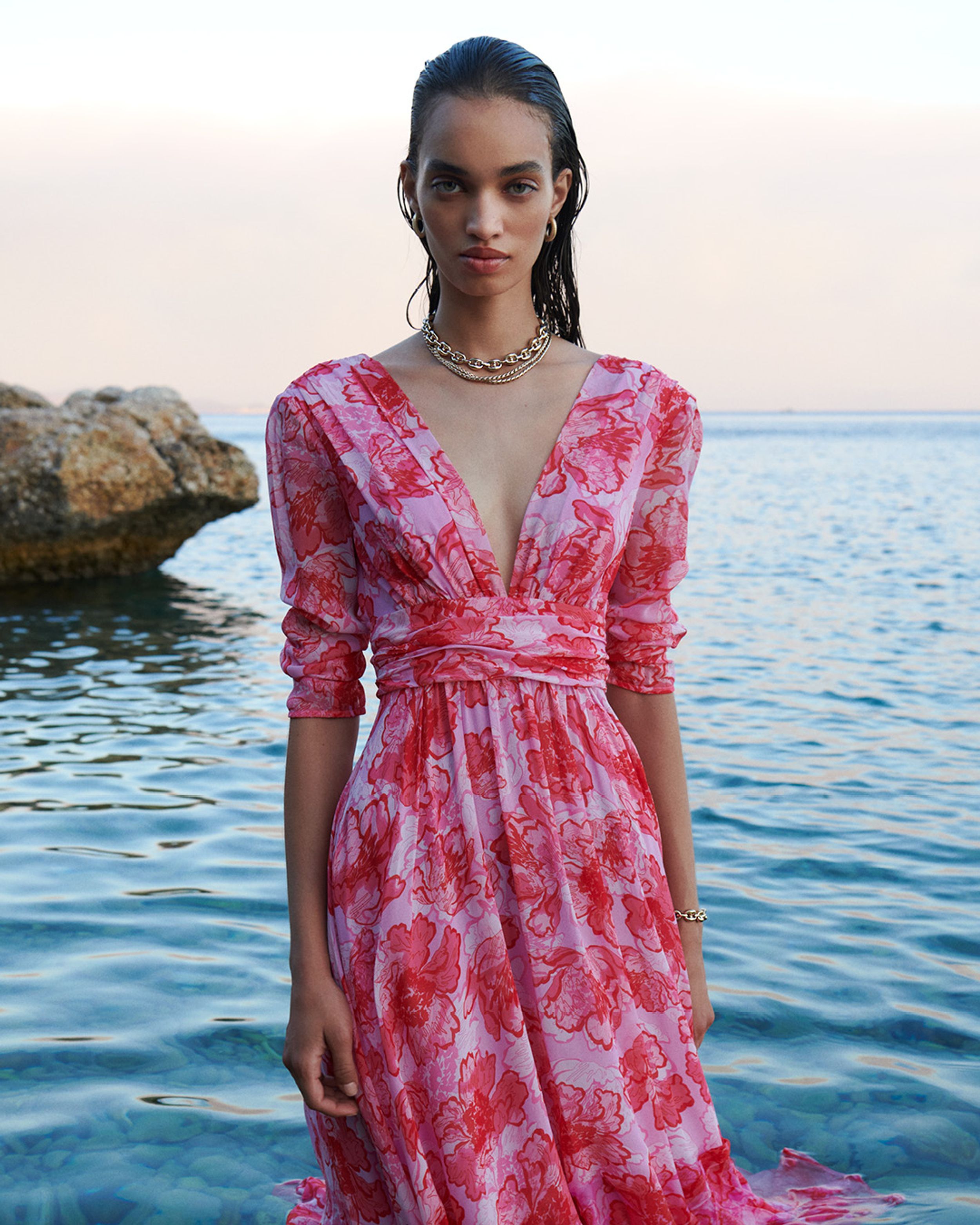 Model standing in the ocean at sunset wearing a pink floral print dress