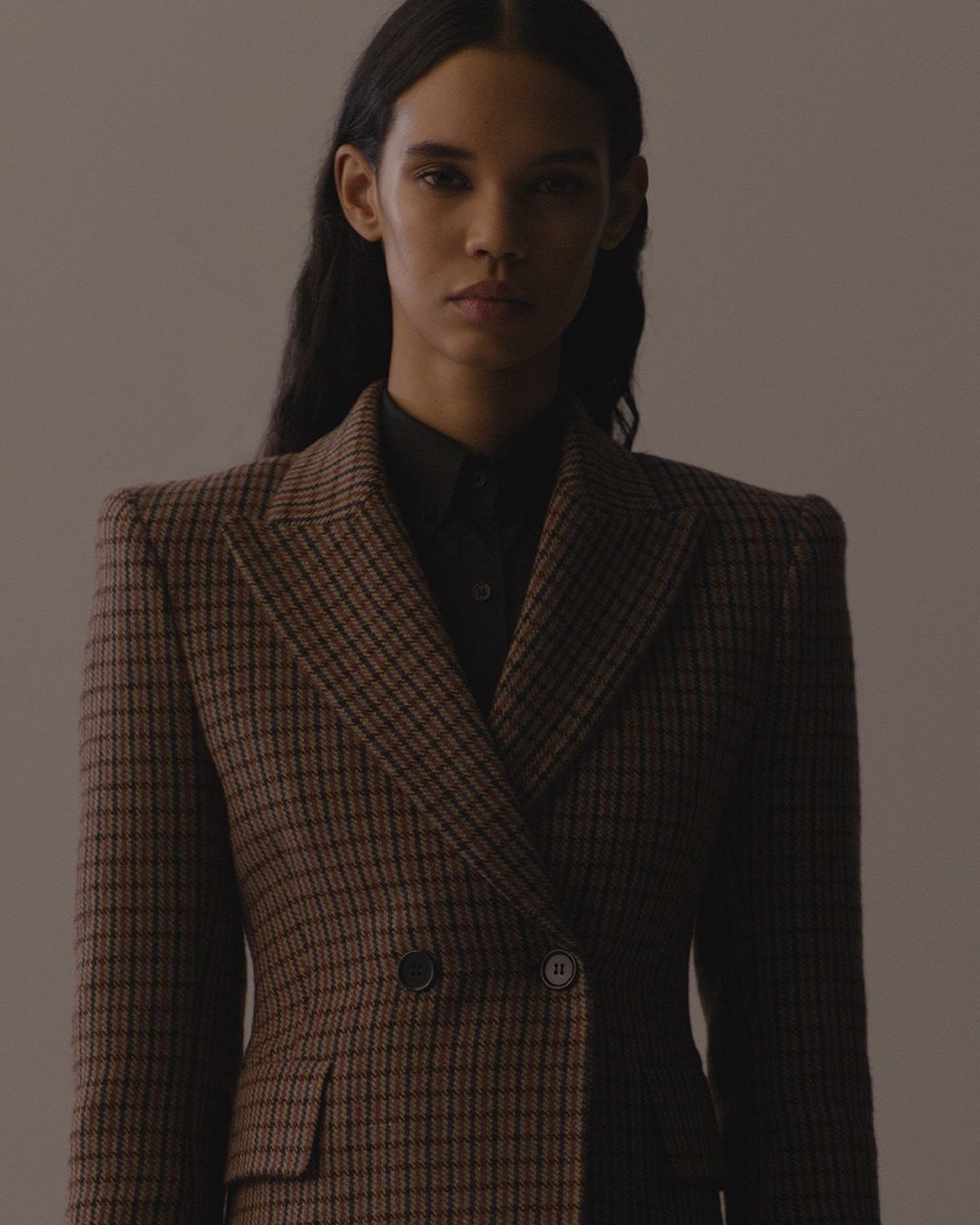 Woman wearing red and brown plaid blazer with shoulder pad dark lighting shadowing right side face.