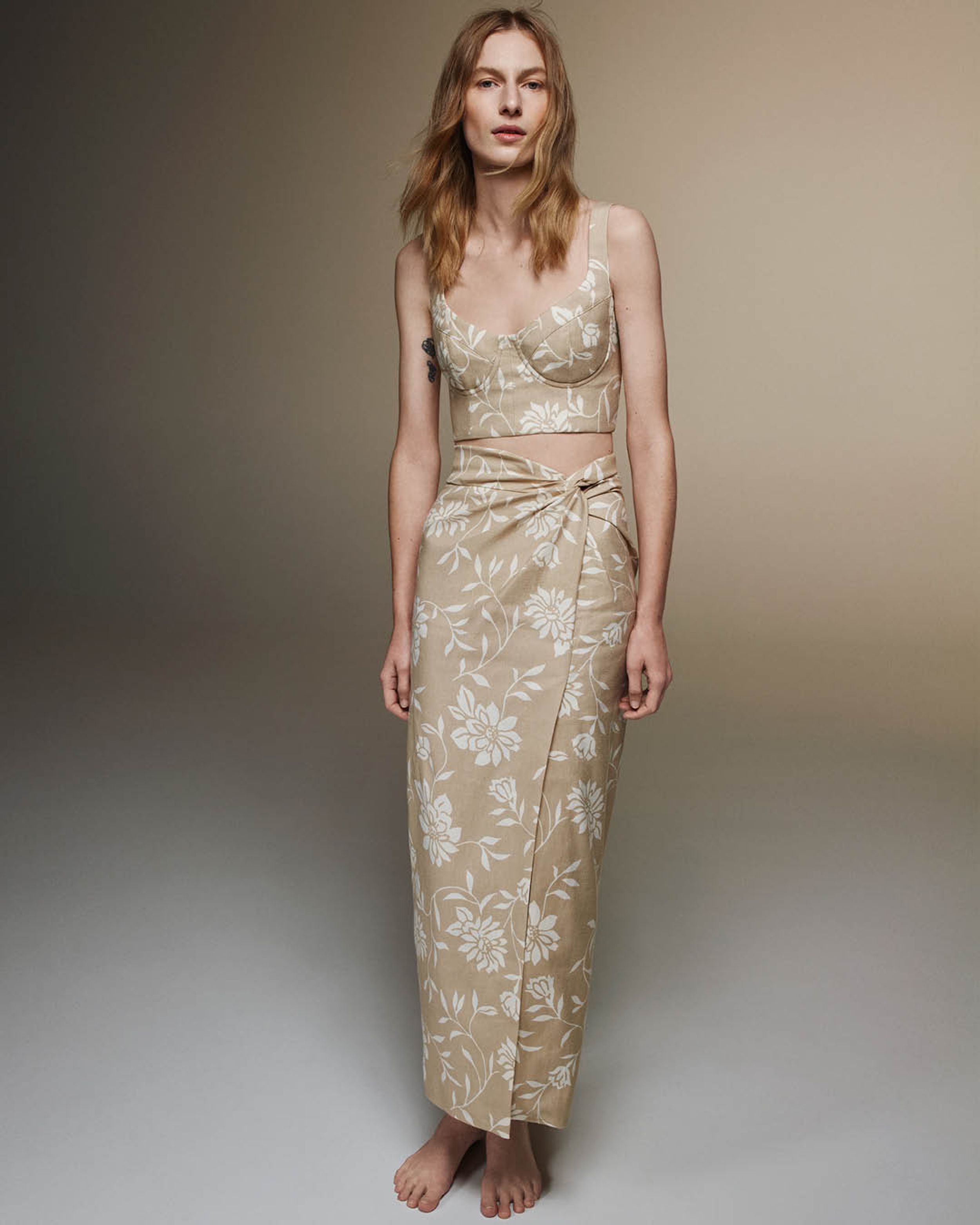 Julia Nobis standing in a matching linen bustier and skirt in beige with white floral print