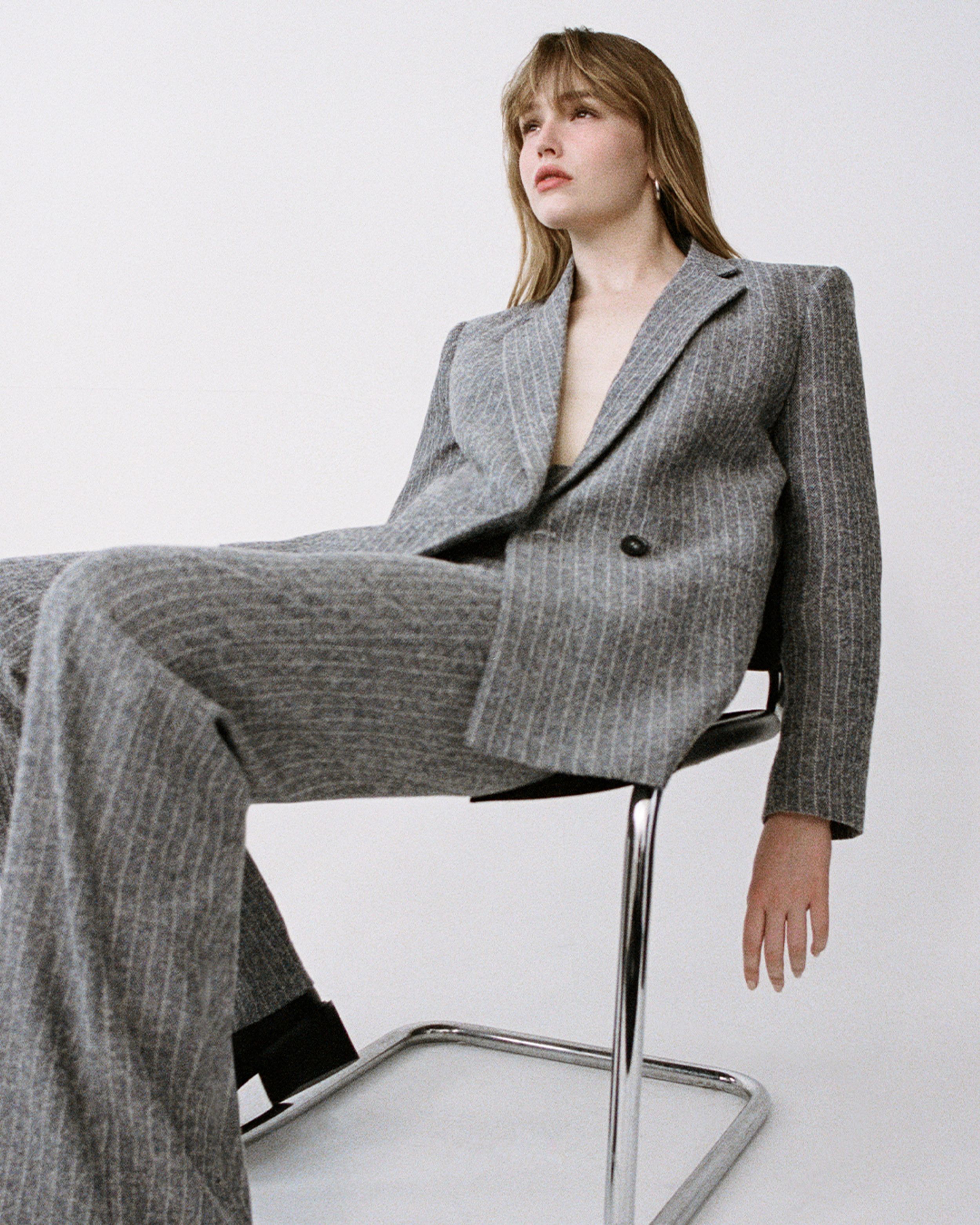 Maddison Brown sitting in a chair wearing a grey pinstripe suit