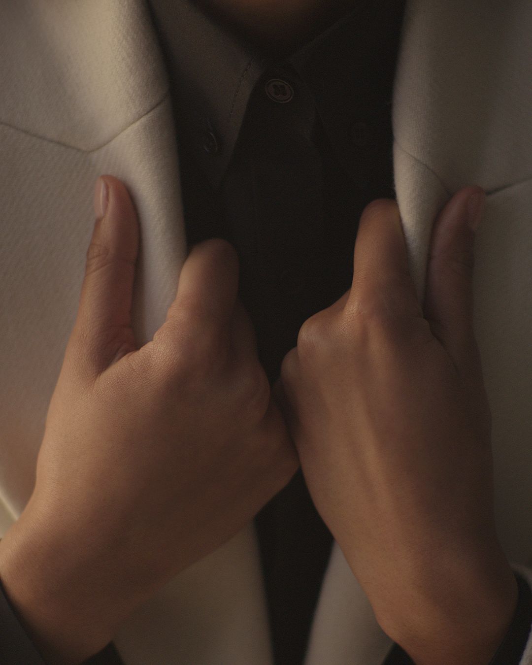 Two hands holding white coat lapel blurred movements on hands dark light with shadow across knuckles.