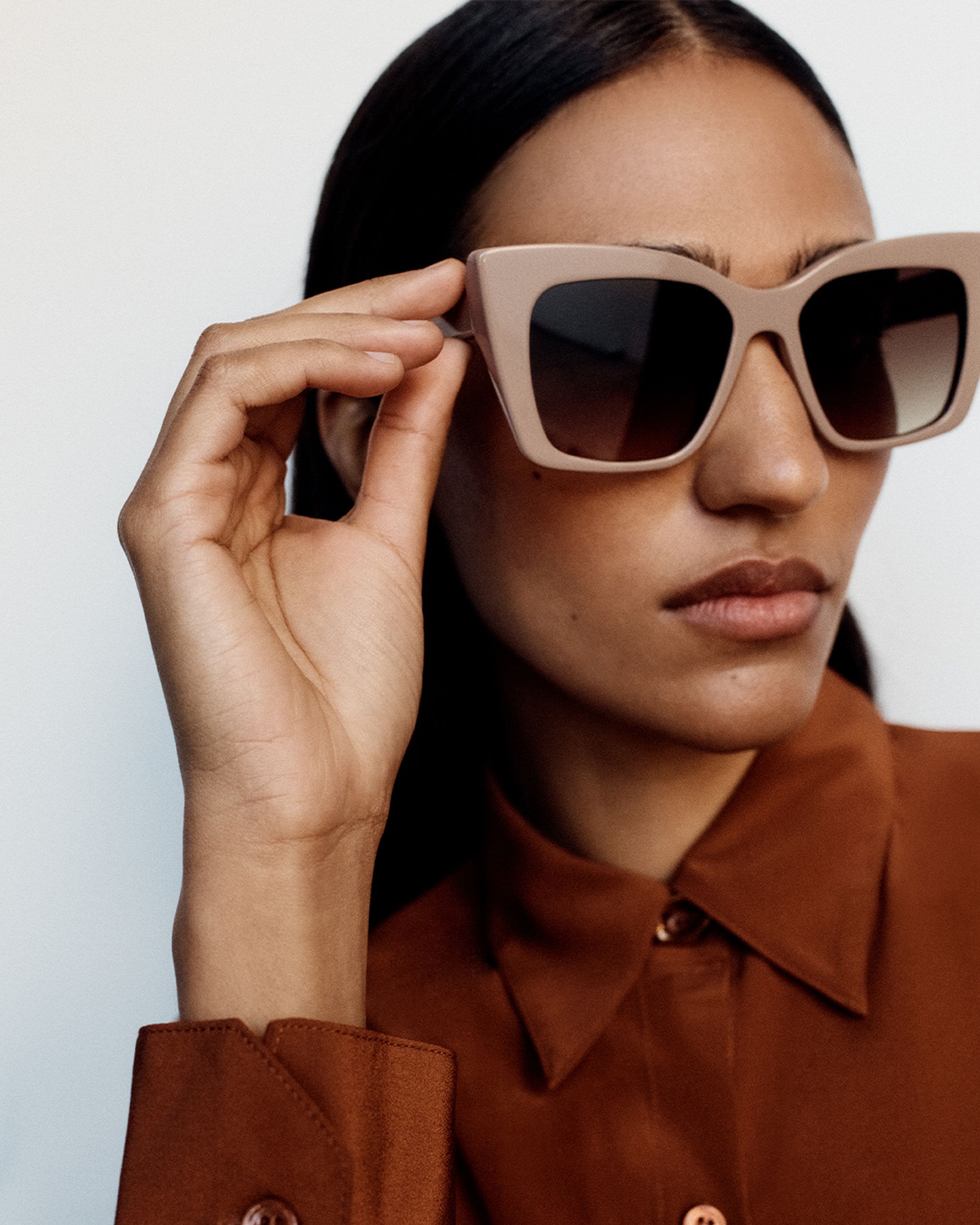 Model looking to the side wearing taupe oversized sunglasses and a rust button up silk skirt