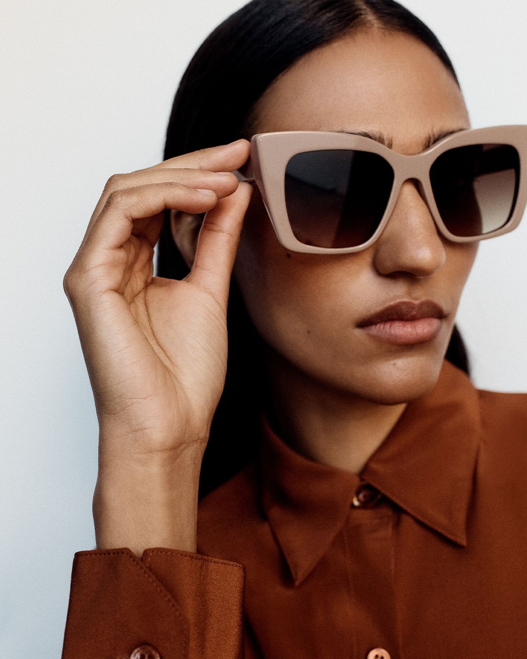 Model looking to the side wearing taupe oversized sunglasses and a rust button up silk skirt