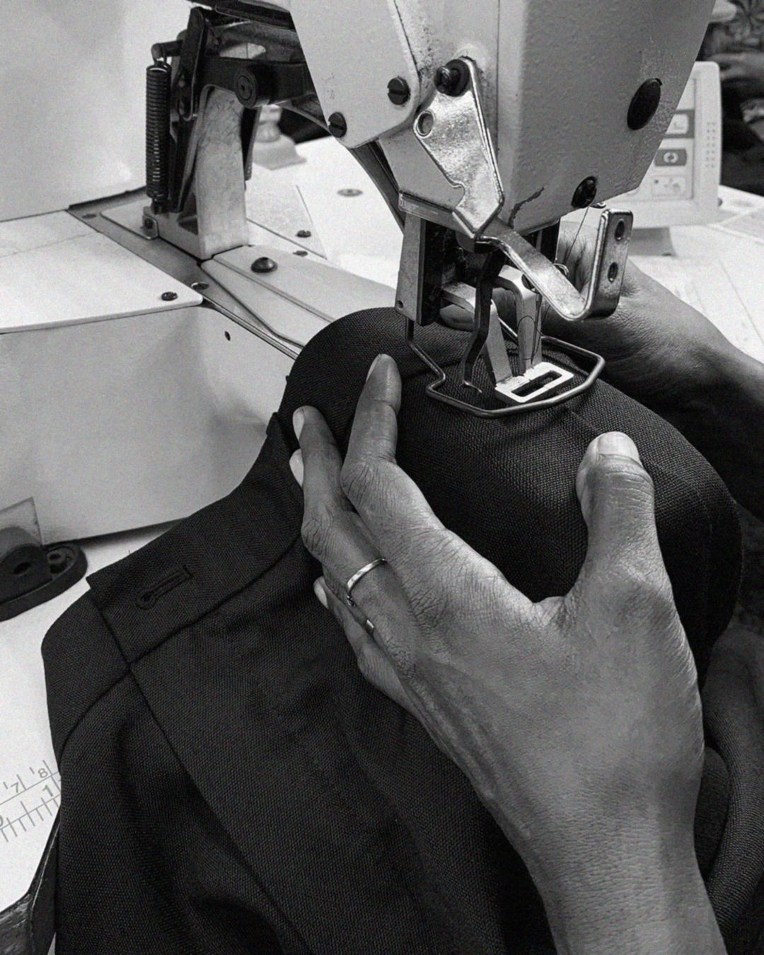 Close up of two hands holding black trousers through a sewing machine