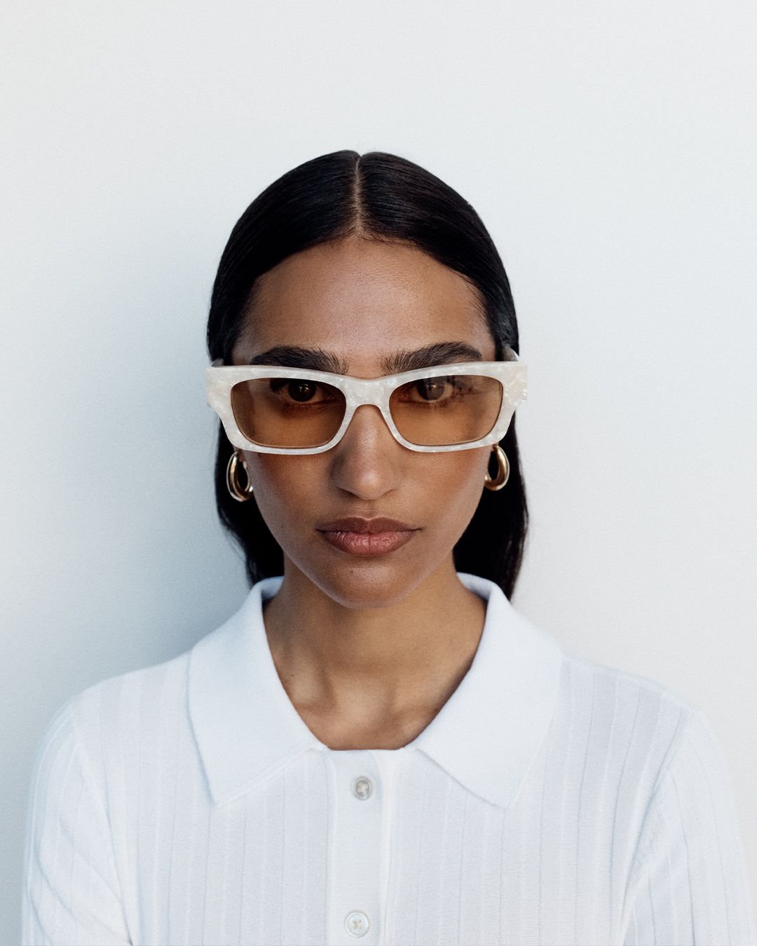 Model gazing at the camera wearing cream-coloured sunglasses with dark brown hair