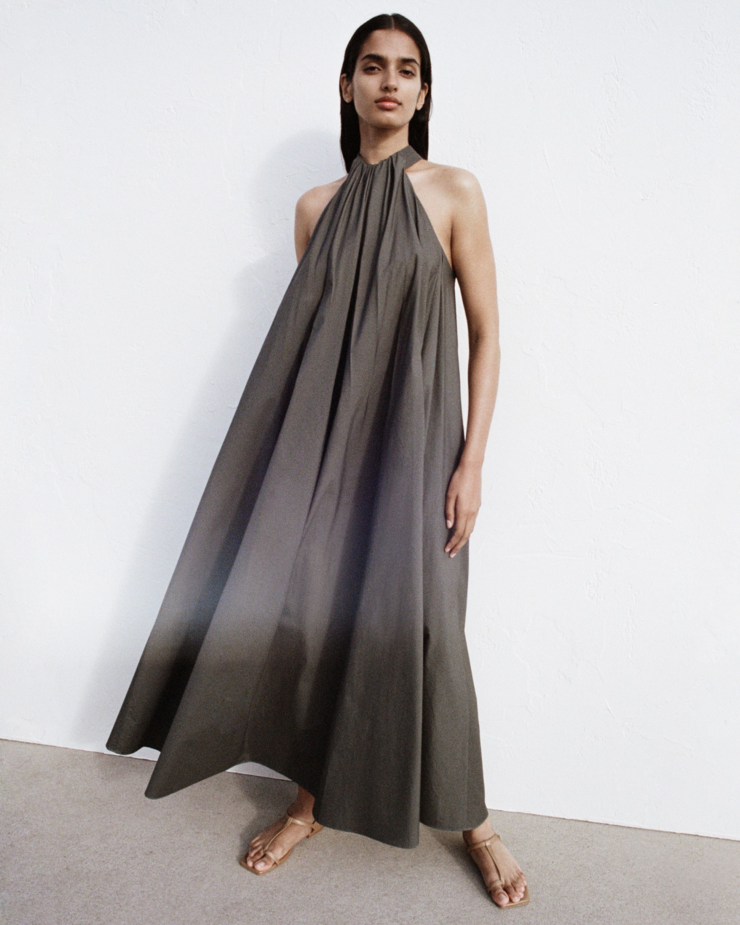 Girl in dark green dress with high neck, with wind blowing through her dress showing pleat detail.  