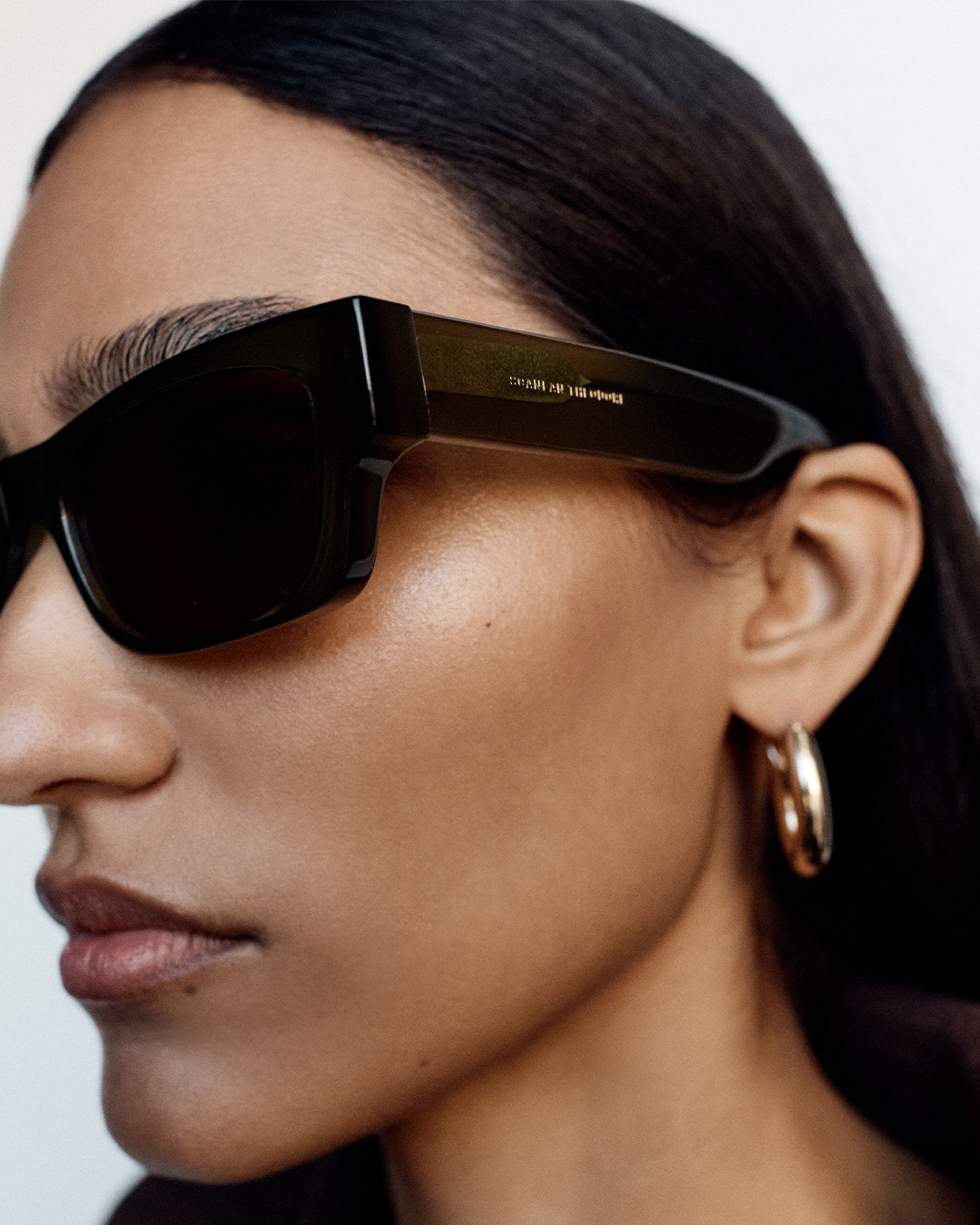 Close up of model's face wearing sunglasses with gold hoop earrings and dark brown hair