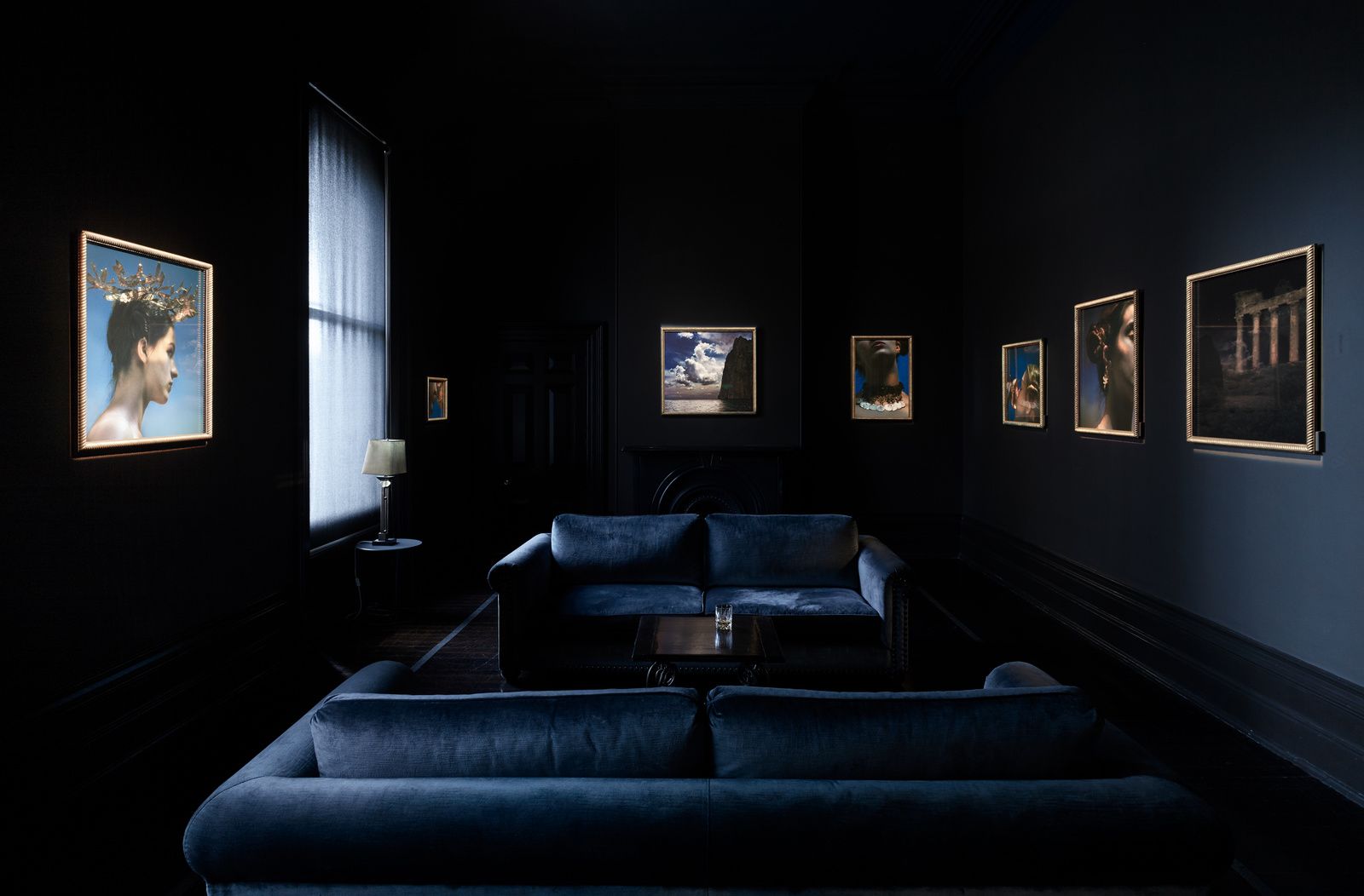 Dimly-lit room with six illuminated framed photographs on the walls with two dark blue sofas