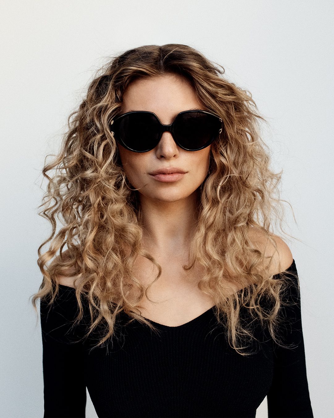 Model with blonde curly hair wearing black round sunglasses