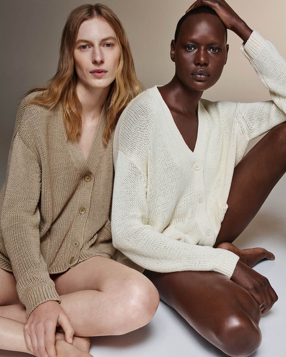 Julia Nobis and Ajak Deng sitting side by side wearing relaxed silk cotton cardigans in taupe and cream