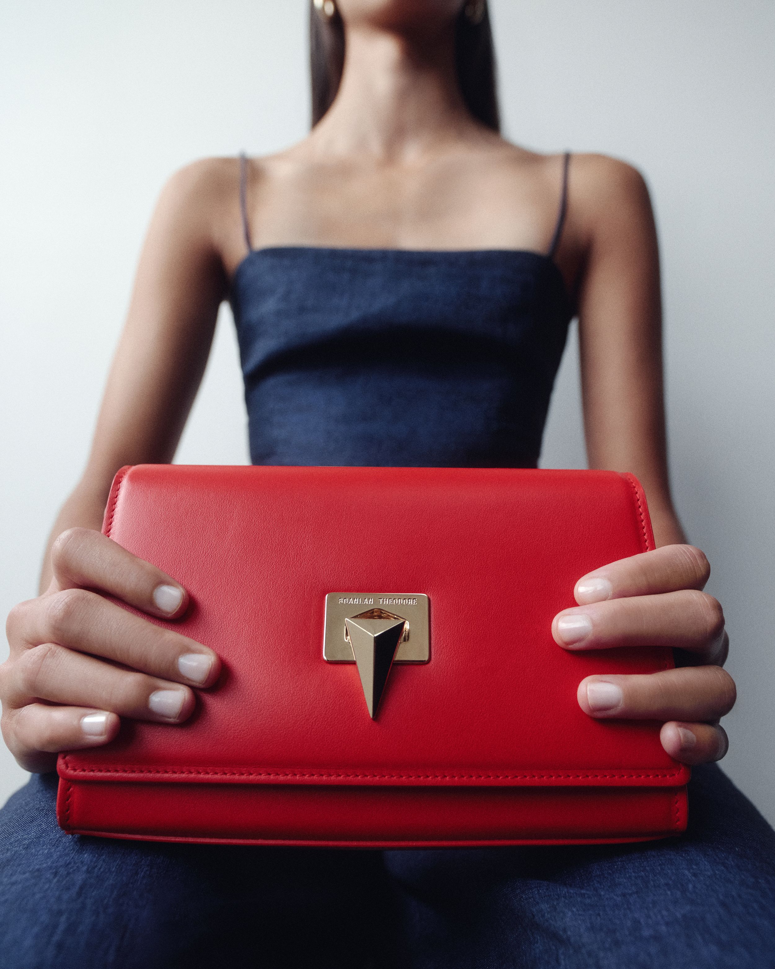 Close up of model holding red leather bag with gold detailing in both hands