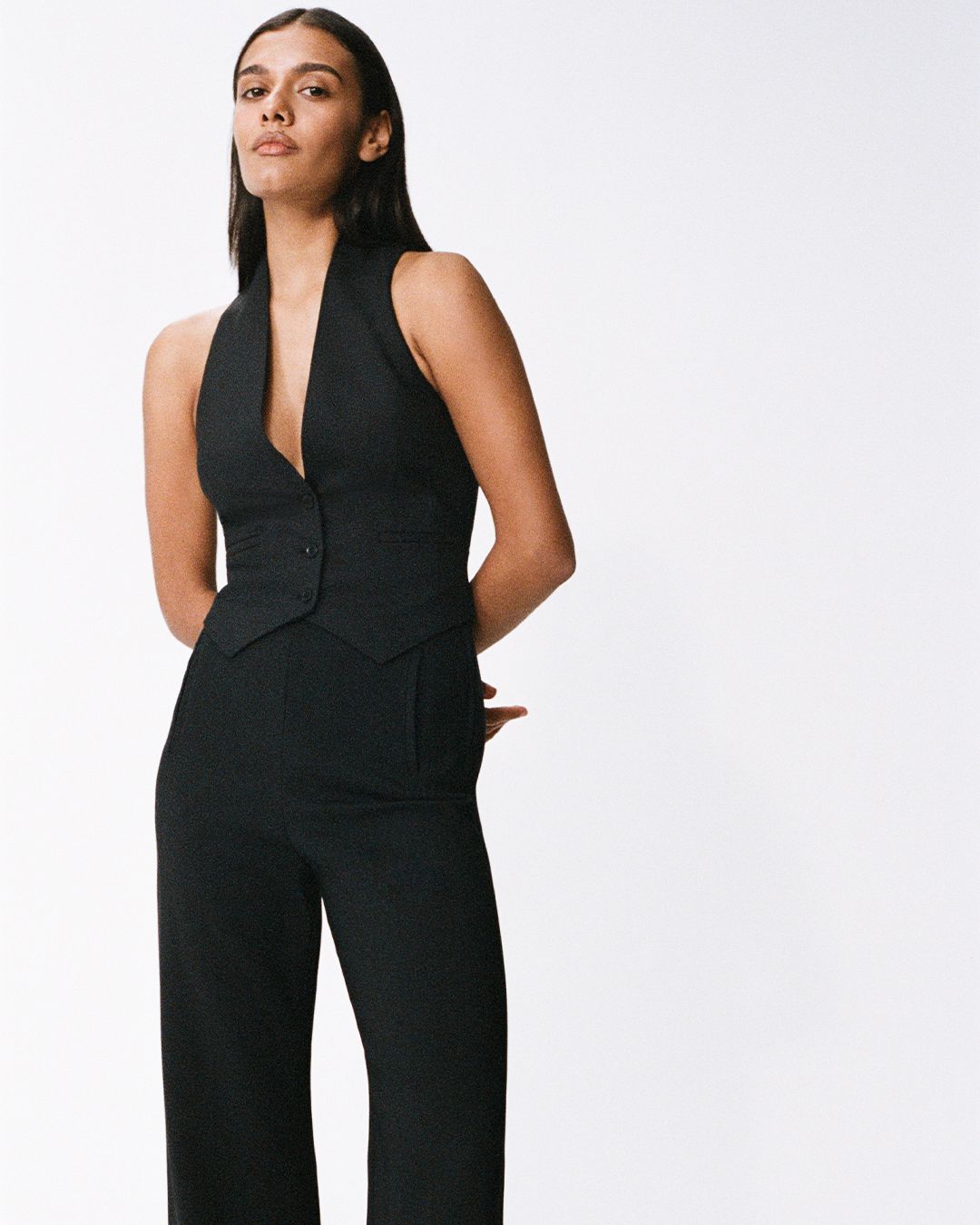 Madeleine Madden standing strong with hands behind her back wearing black tailored twill vest and high waisted trousers