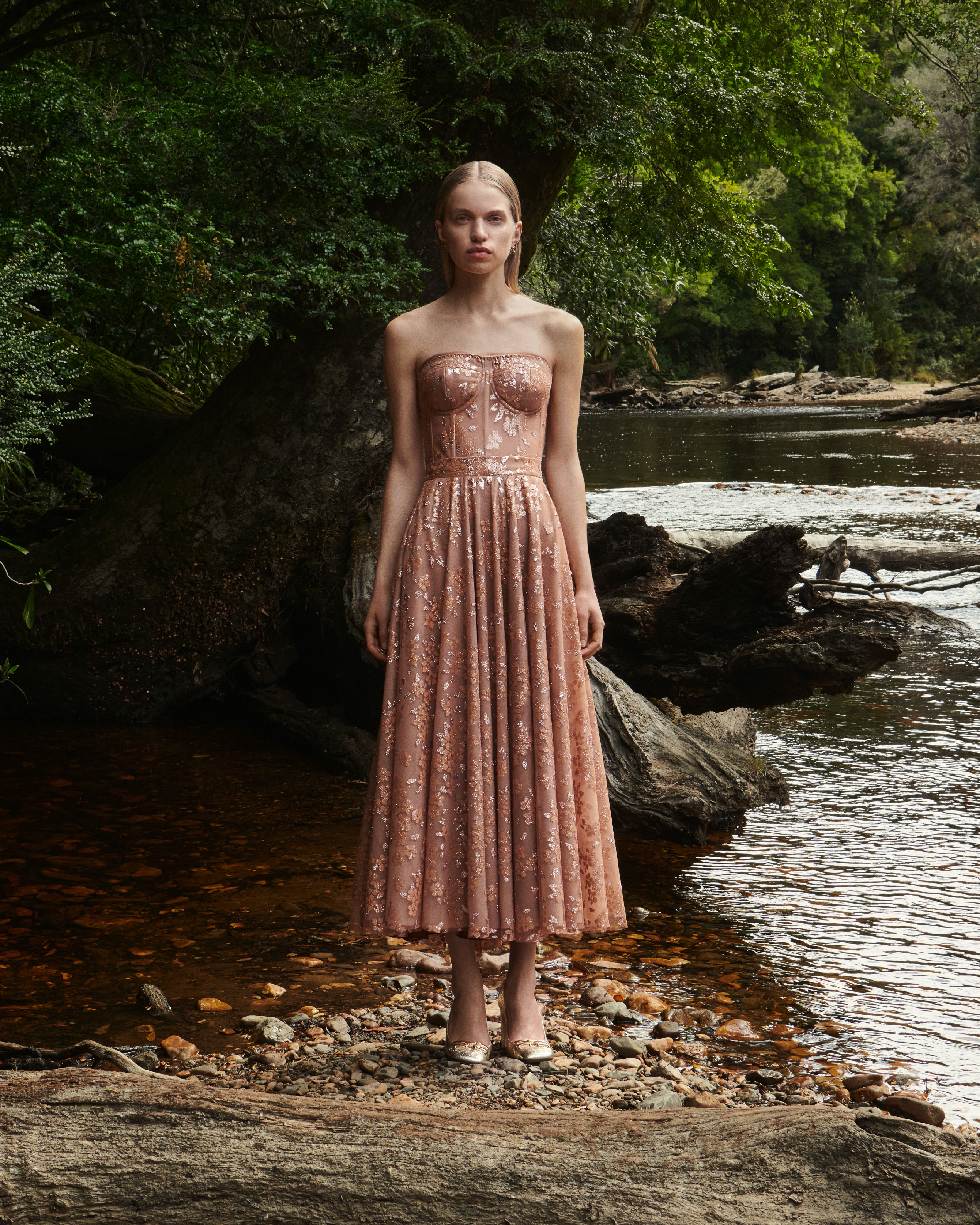 Two images side-by-side of Sabine Glud wearing a shimmery apricot bustier and skirt sitting in the forest (left) and standing by the river (right)