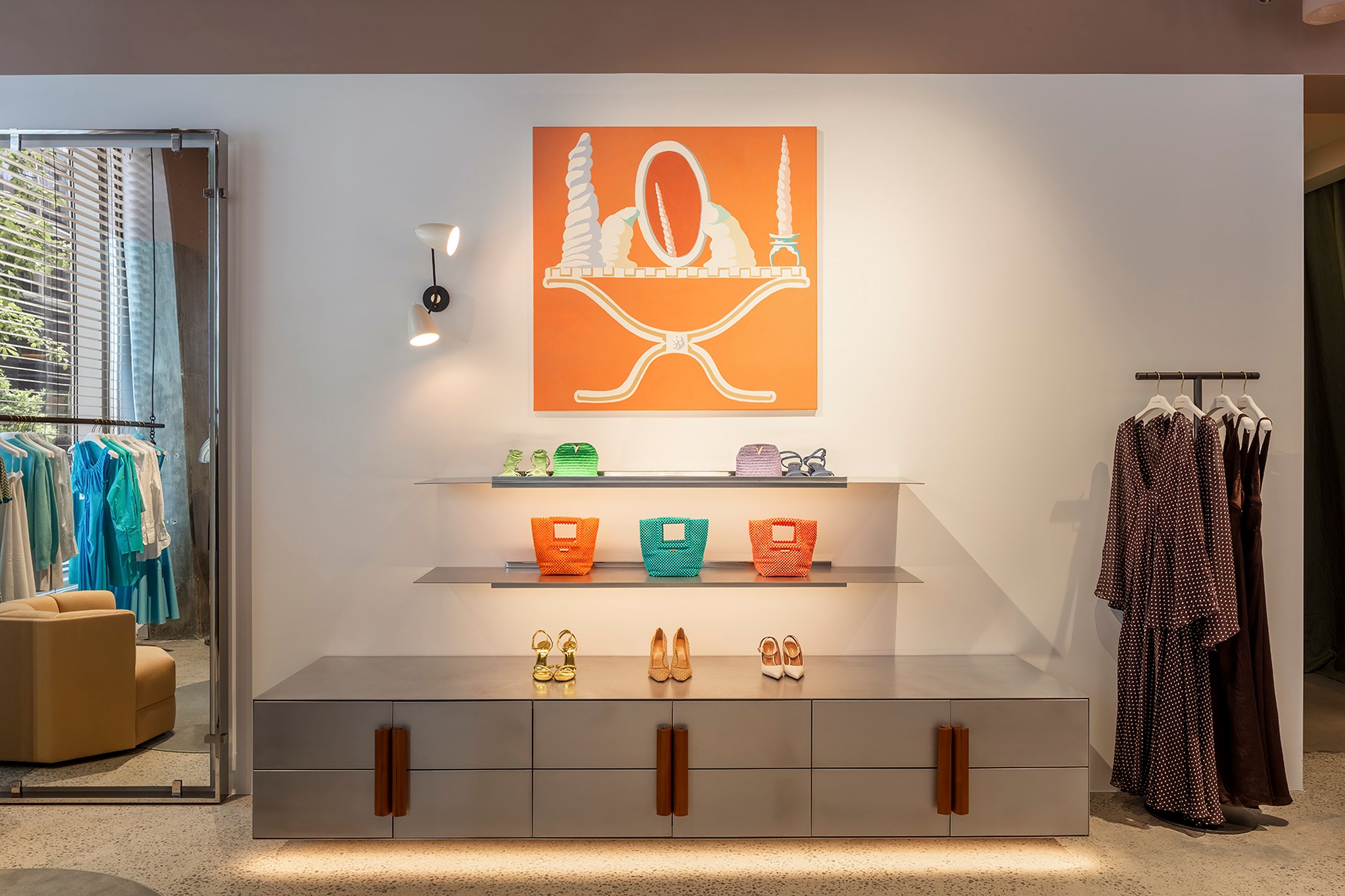 Shelves displaying brightly-coloured shoes and bags, with a bright orange painting above