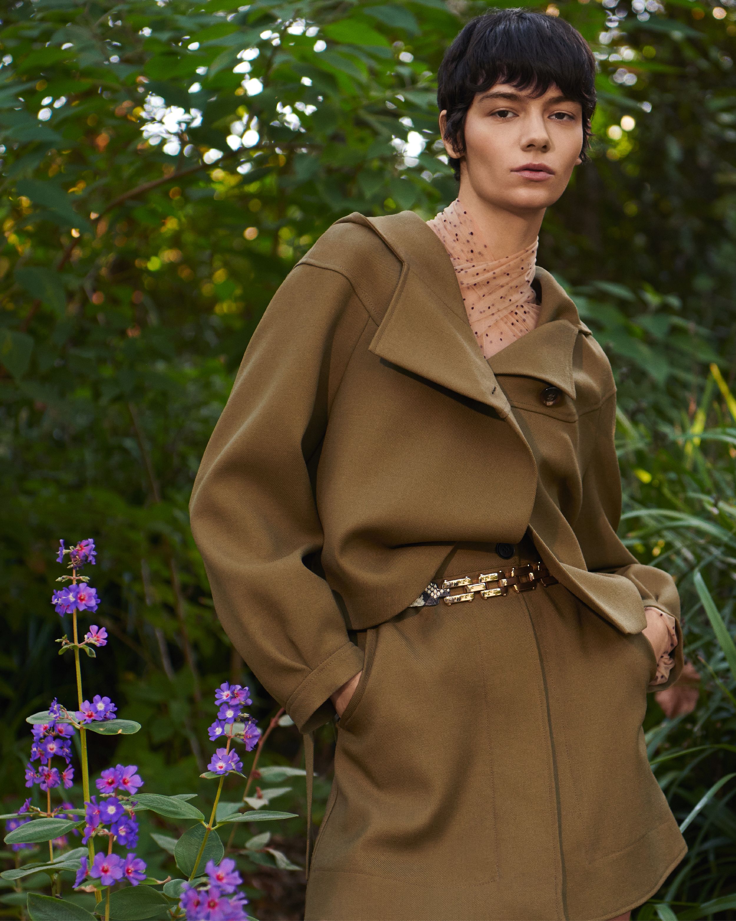 Mid shot of model standing outdoors wearing a matching khaki cropped jacket and mini skirt