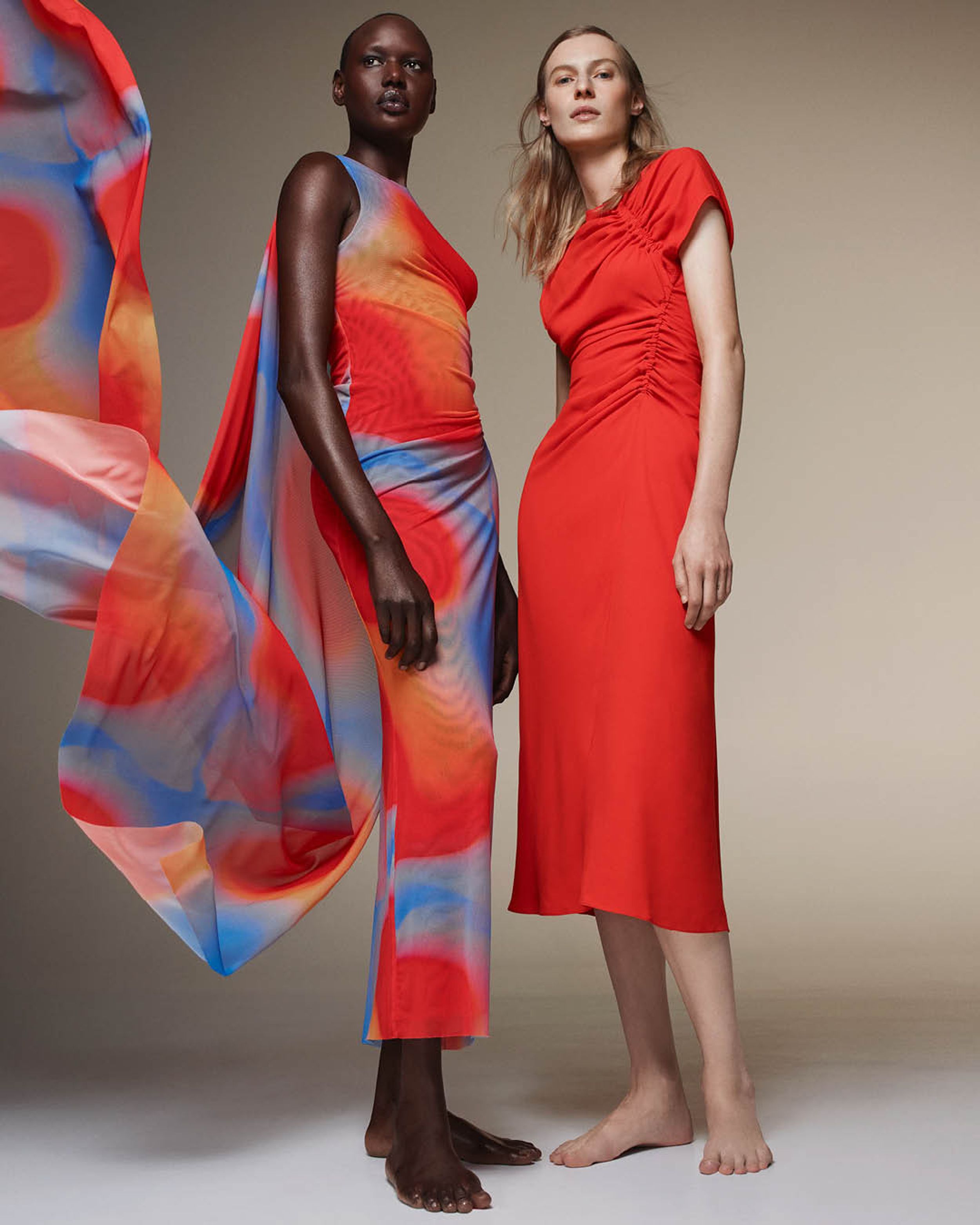 Ajak Deng wearing a mesh orange and red dress standing beside Julia Nobis wearing a gathered orange dress 