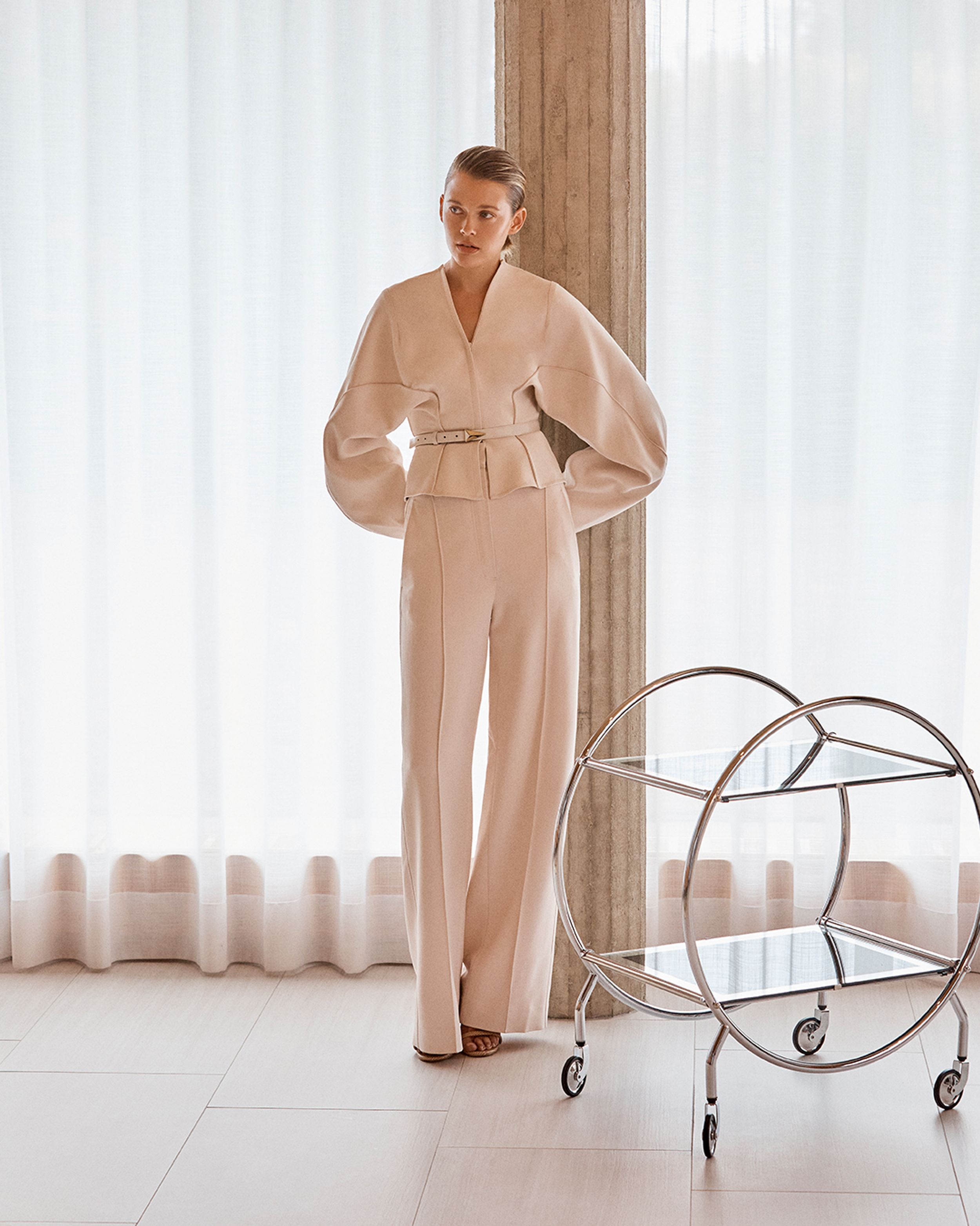 Model leaning against a pillar wearing a cream-coloured top and trousers