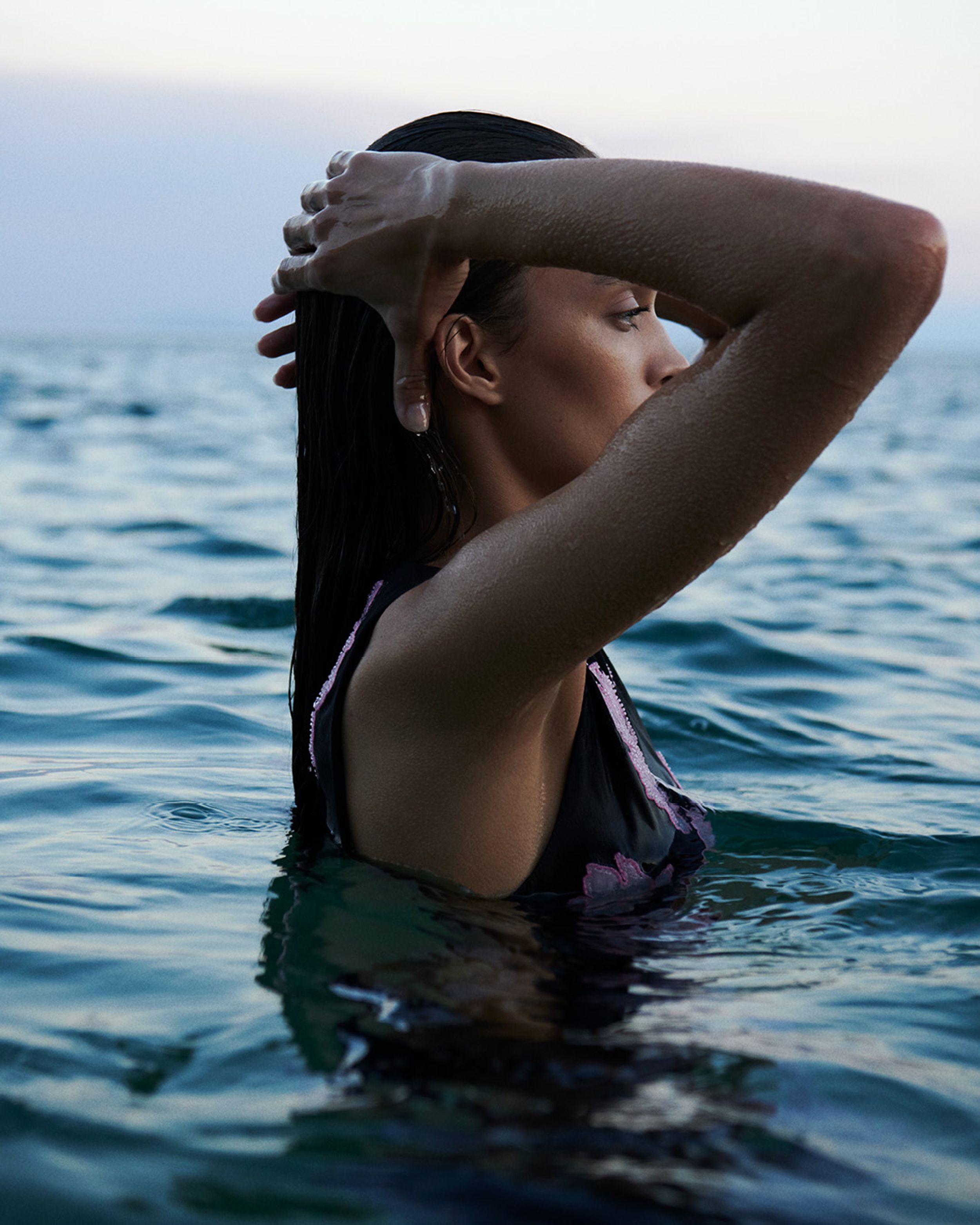 Model standing in the ocean with heads on hand wearing a black dress with embroidered pink flowers