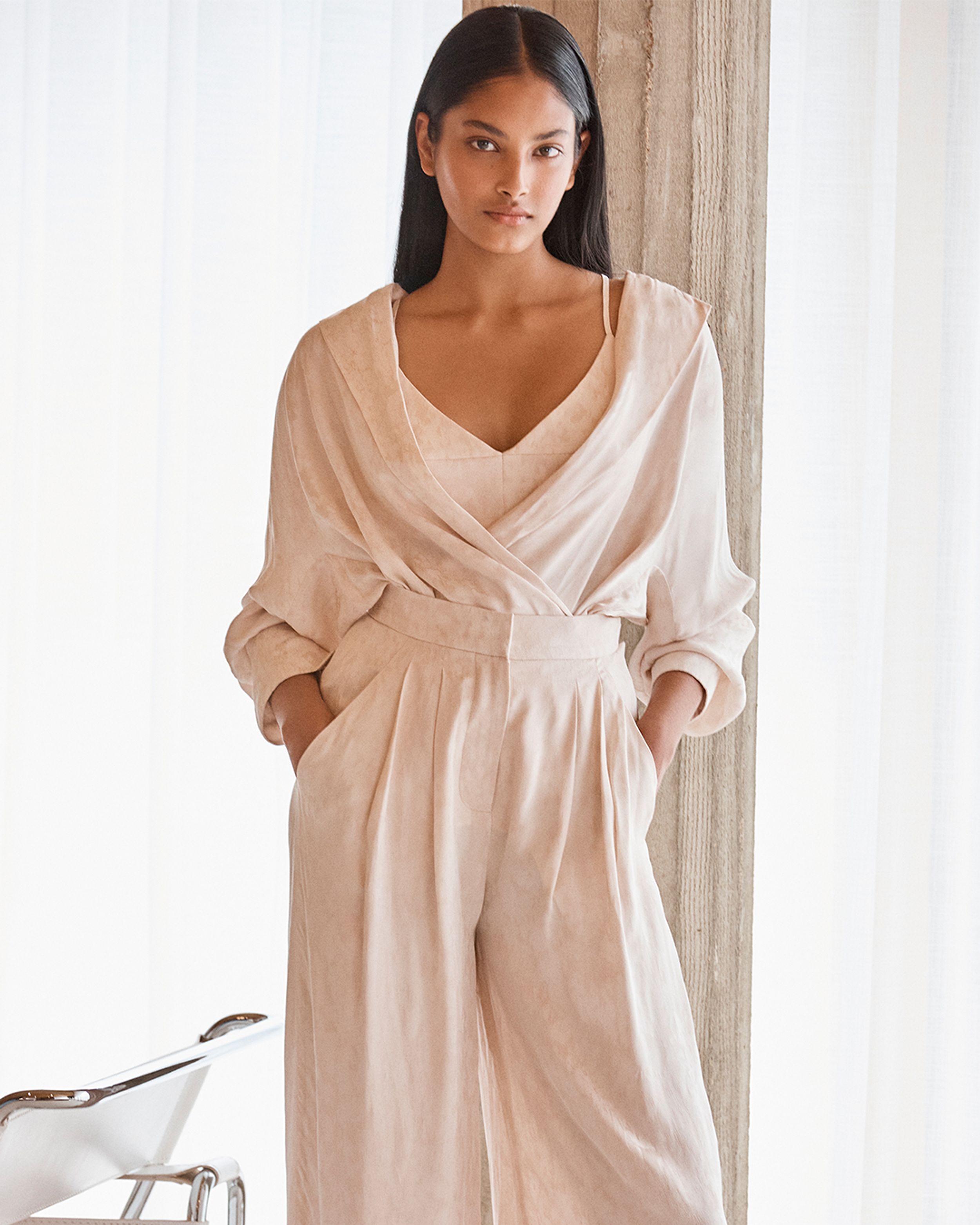 Brunette model leaning on a pillar wearing a cream-coloured shirt and trousers