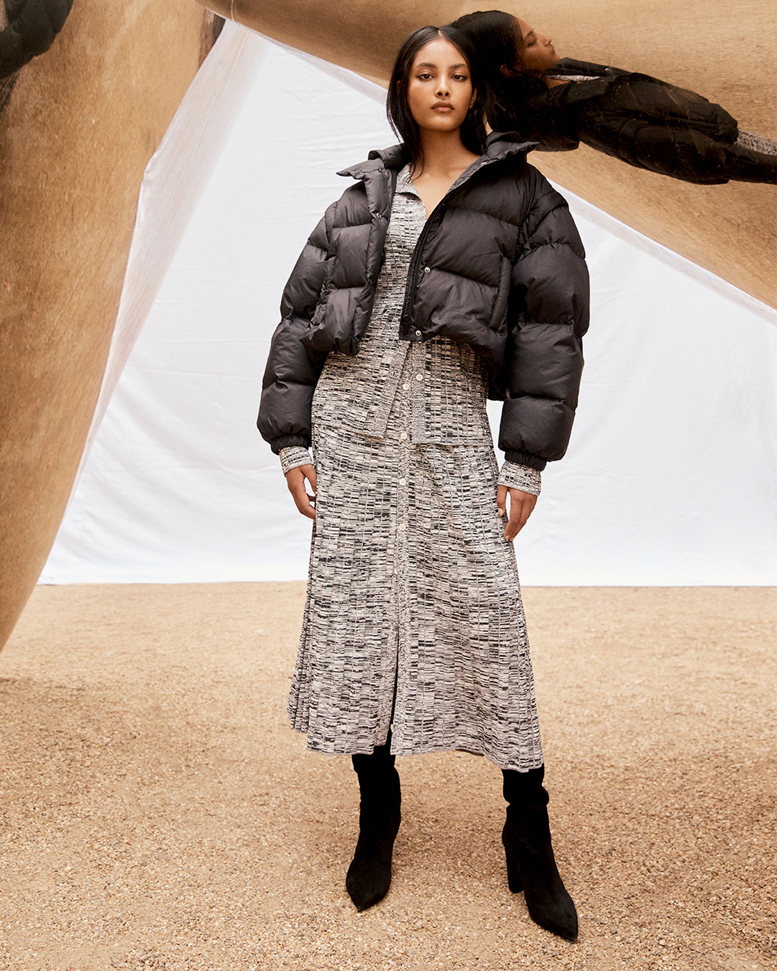 Brunette model standing wearing black puffer jacket and black grey marle rib knit dress