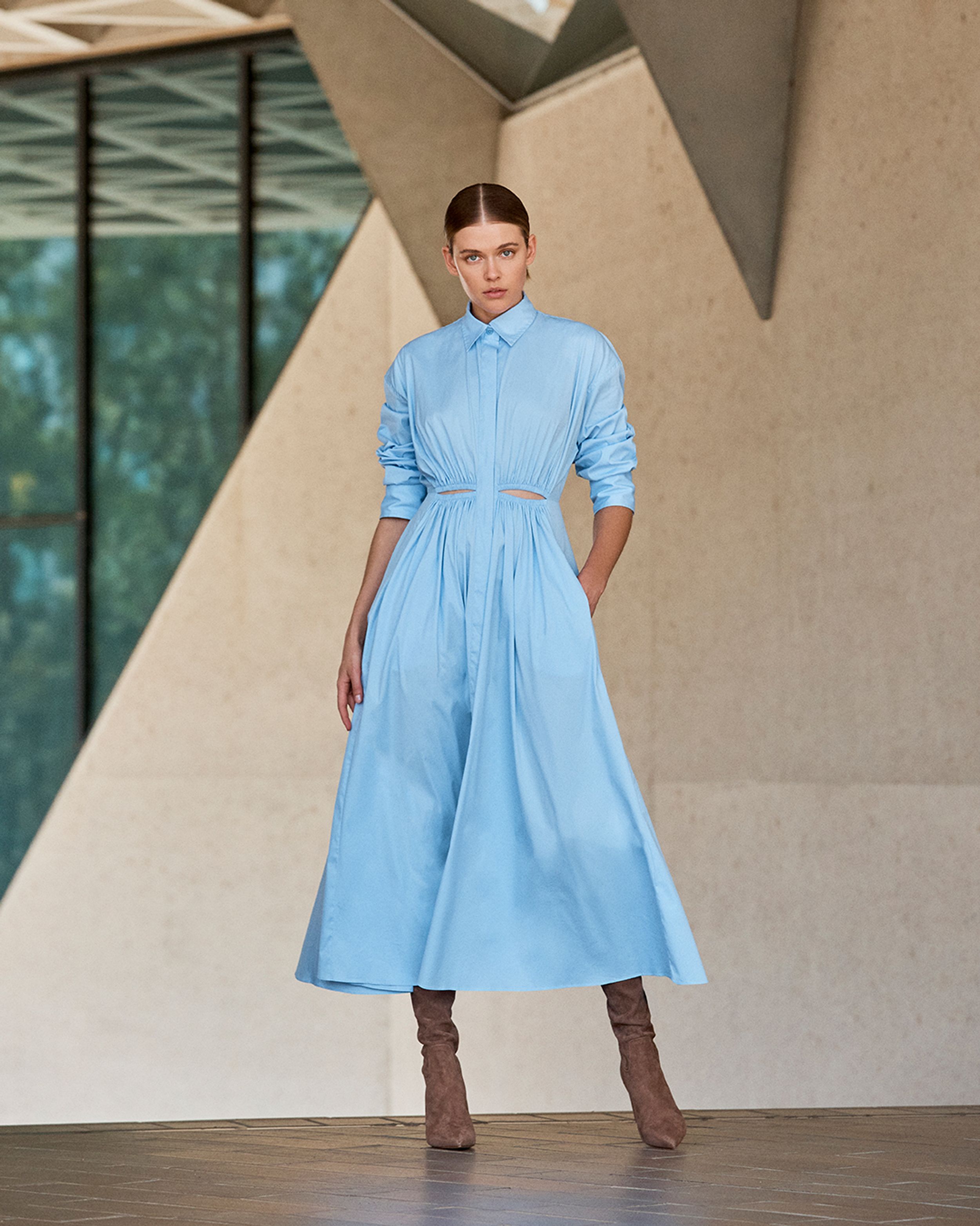 Brunette model standing with a hand in pocket wearing a light blue cotton shirt dress