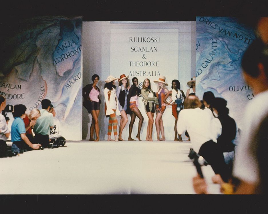Eight models posing on the runway posing in a line with photographers at the sides