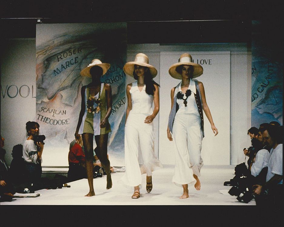 Three models walking side by side down the runway wearing straw sunhats and white clothing
