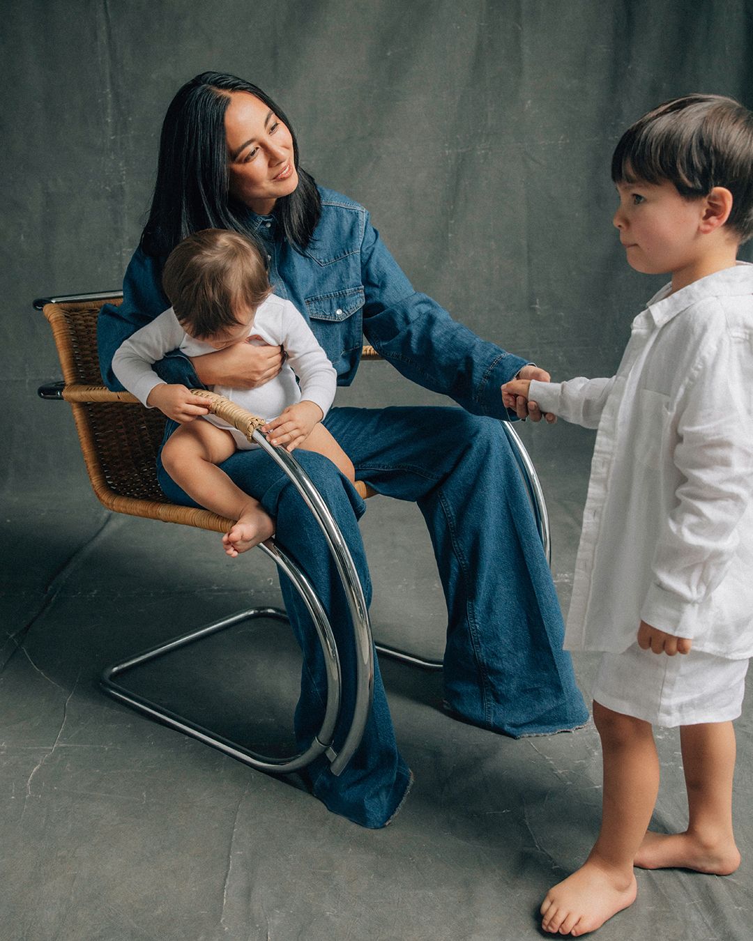 Petta Chua in double denim sitting down holding her baby while holding her toddler's hand