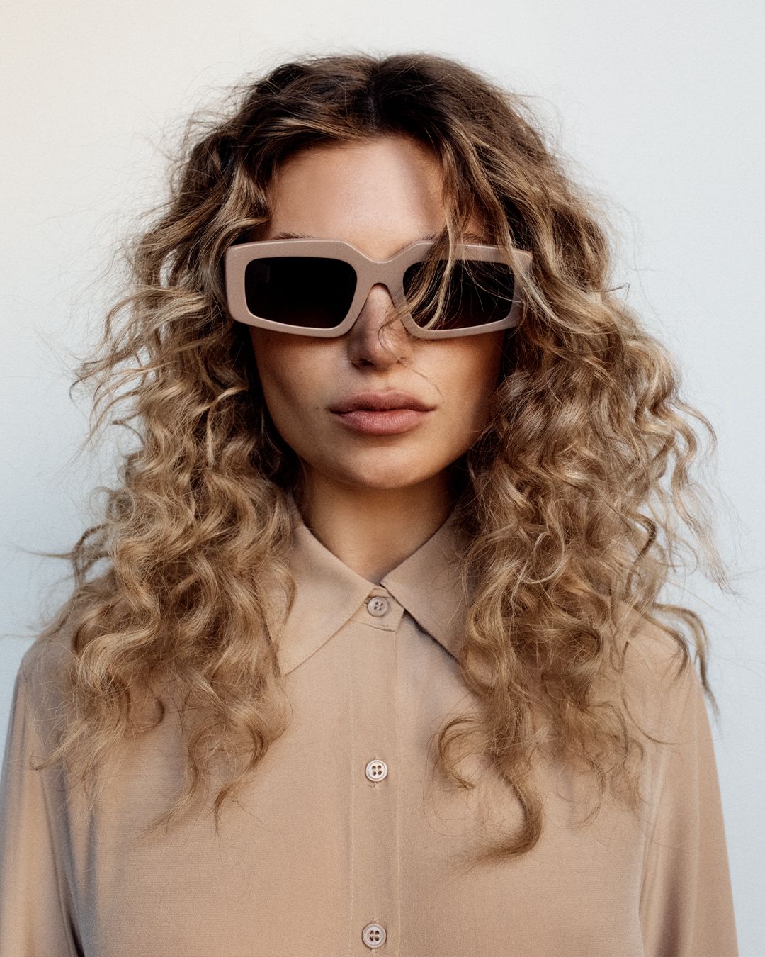 Model wearing taupe rectangular sunglasses with a taupe silk shirt