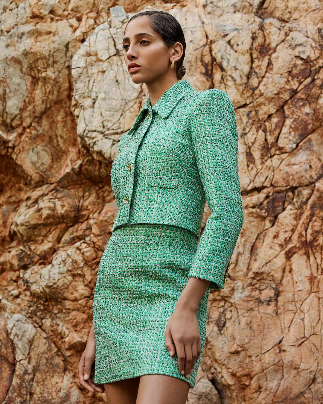 Yasmin Wijnaldum standing facing the side wearing a matching green tweed jacket and mini skirt