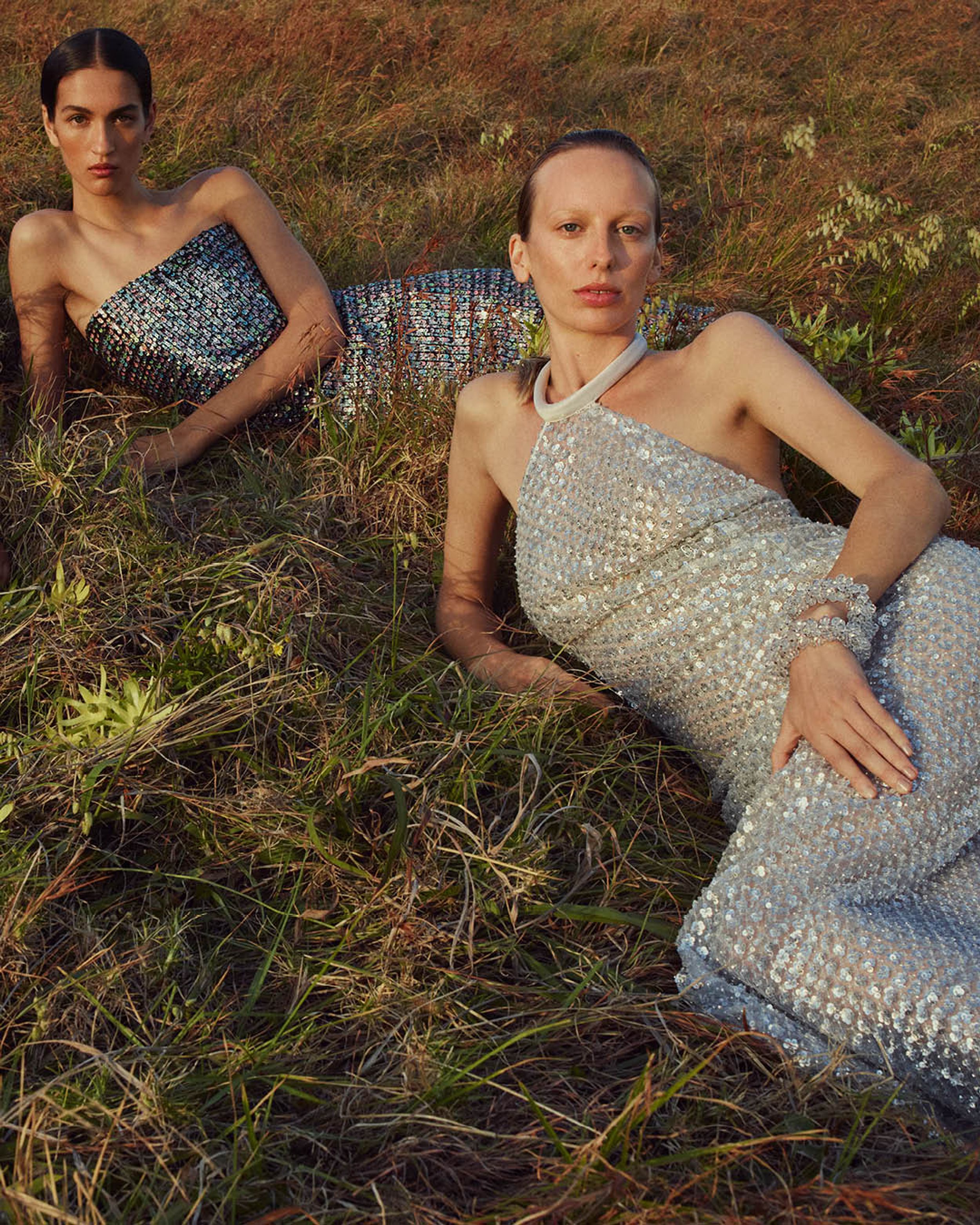 Two models lying on the grass wearing violet and silver evening gowns