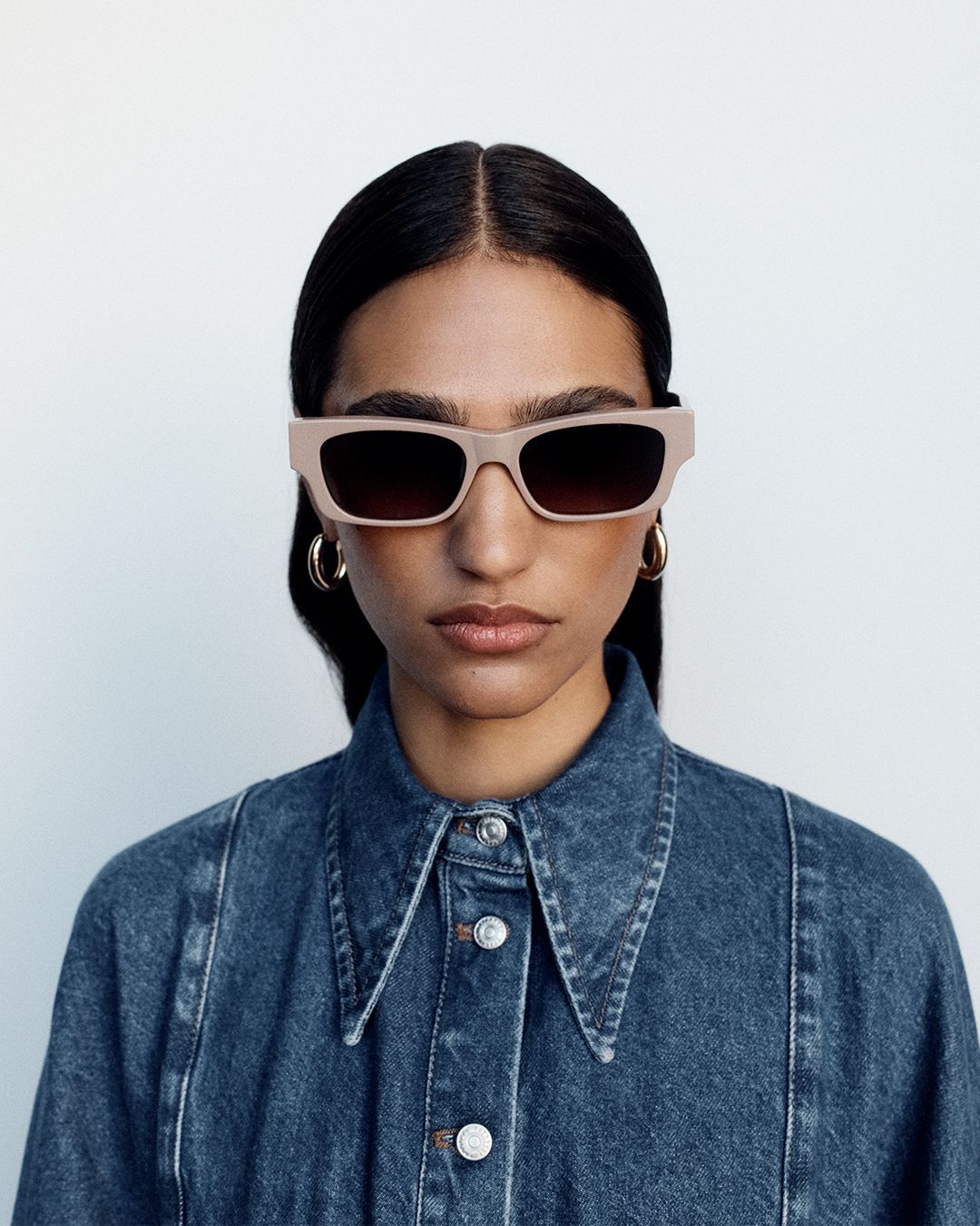 Model wearing taupe sunglasses with a dark blue denim skirt