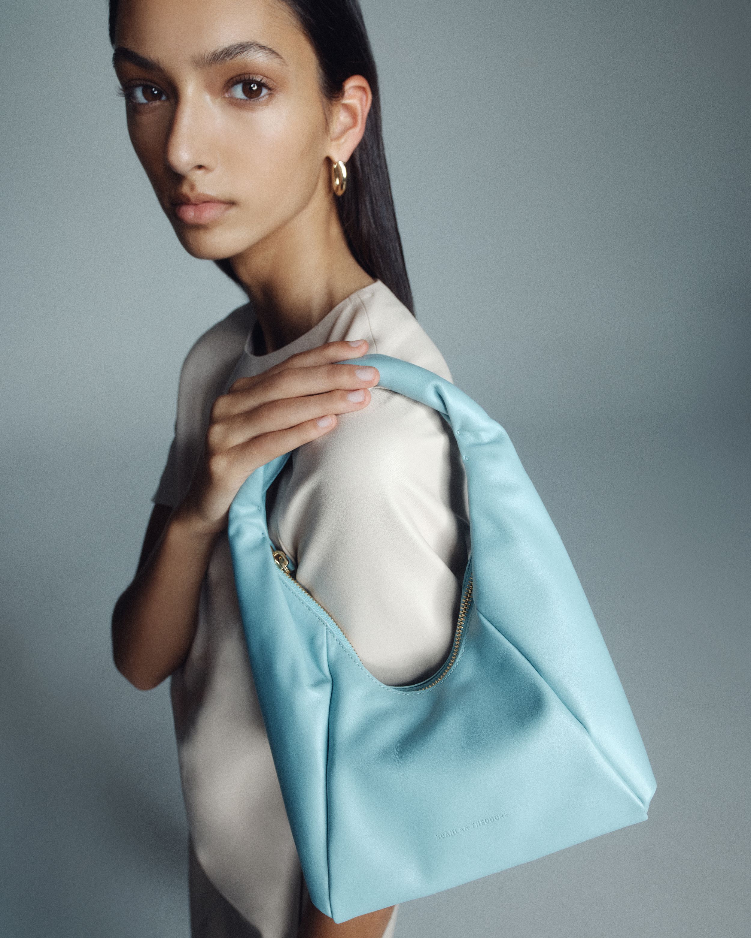 Model holding a light blue leather bag over her shoulder wearing a light taupe leather top