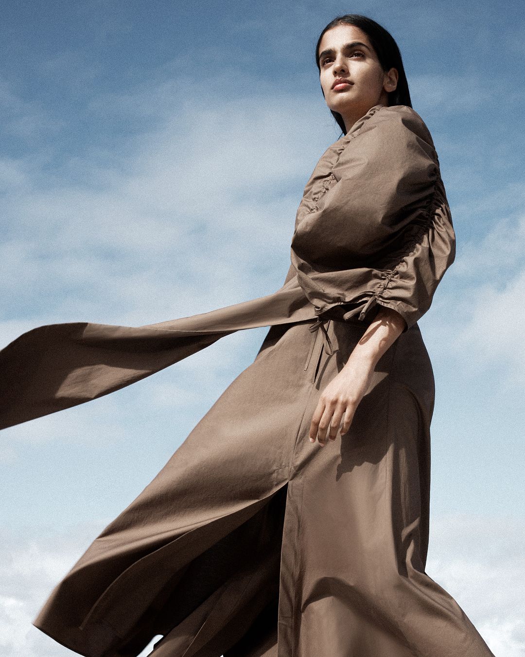 Low angle shot of girl with wind blowing her dress, and blue sky and clouds in the background.