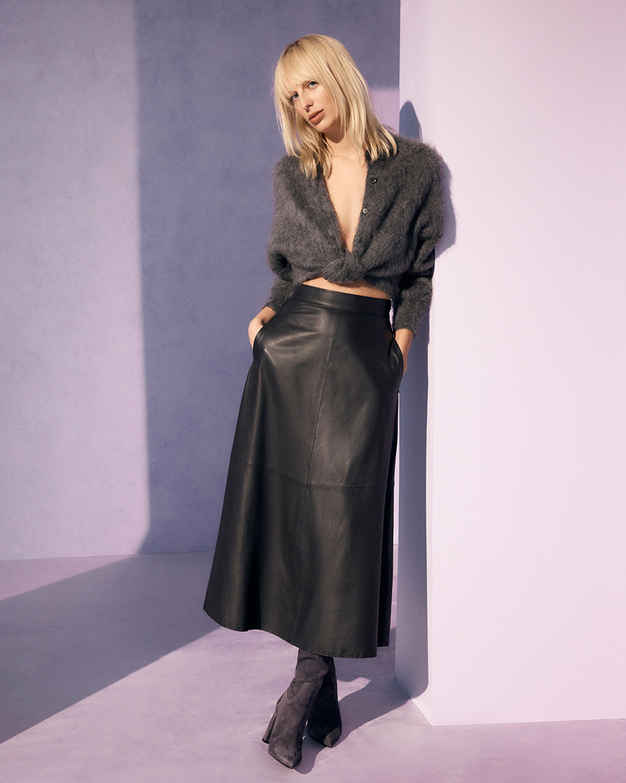 Blonde model standing wearing a grey mohair cardigan and black leather skirt