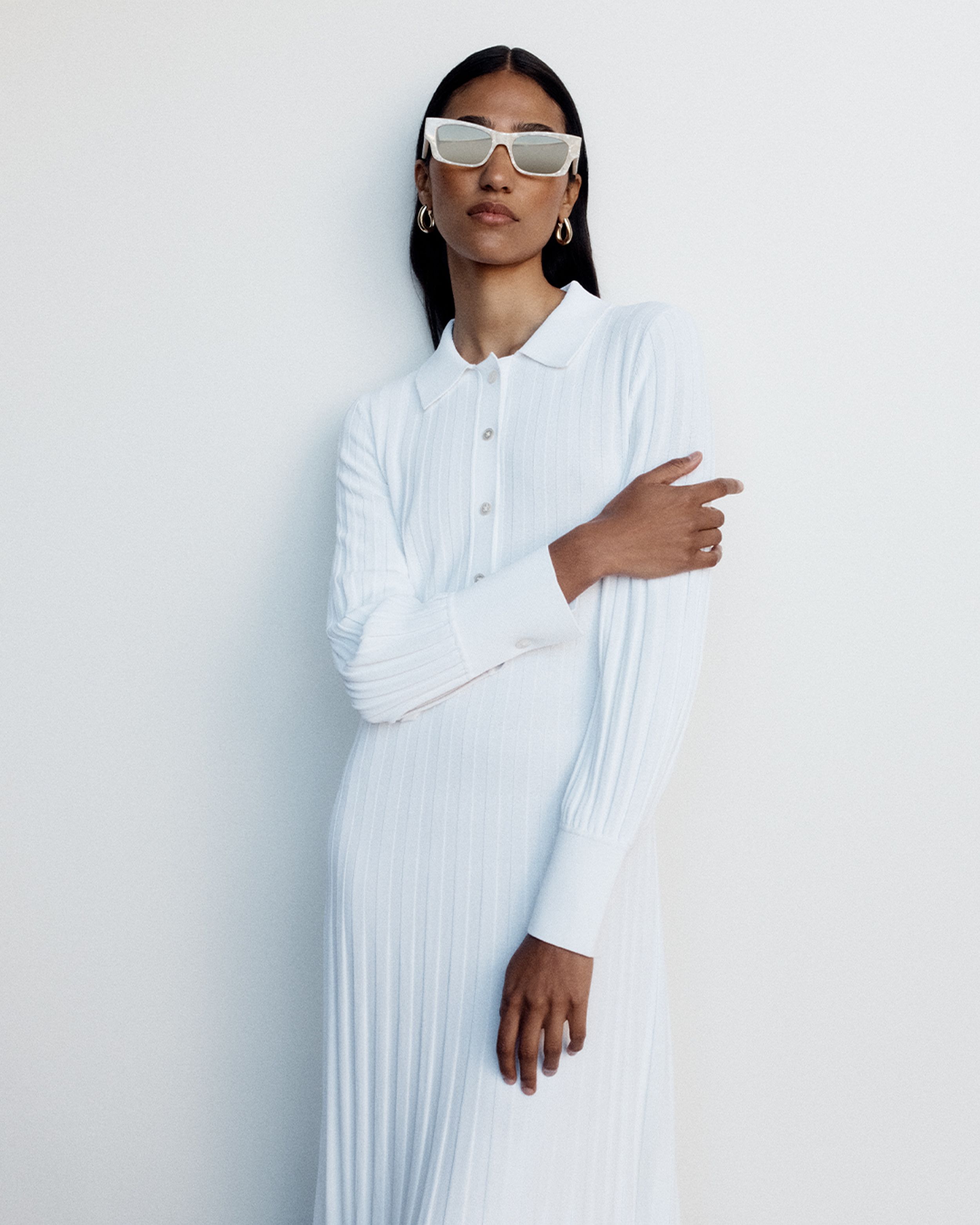 Model wearing cream-coloured sunglasses and a white knitted shirt dress