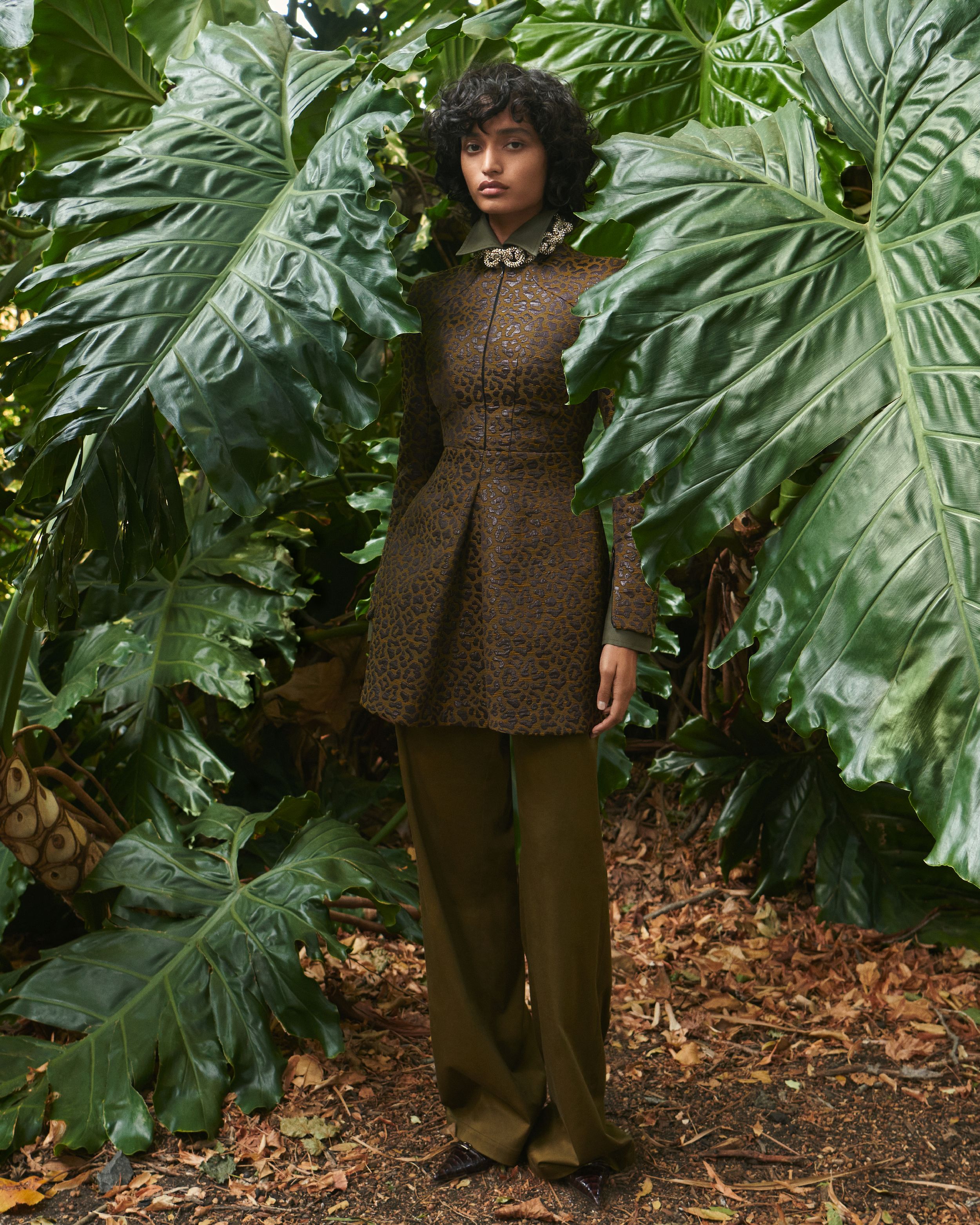 Model standing between large leaves wearing an brown ocelot-print dress brown trousers