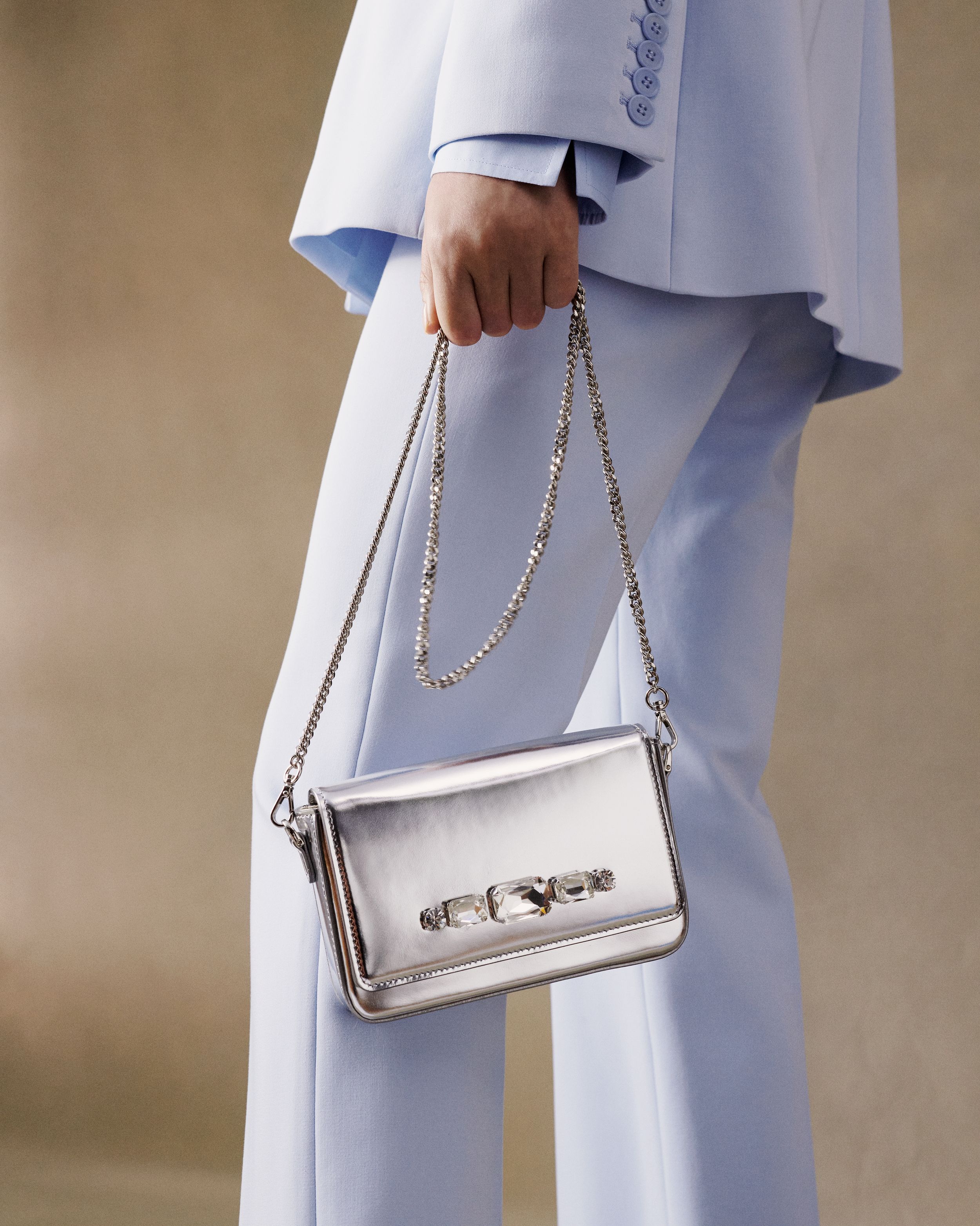 Silver leather bag being held by a model wearing a matching light blue suit