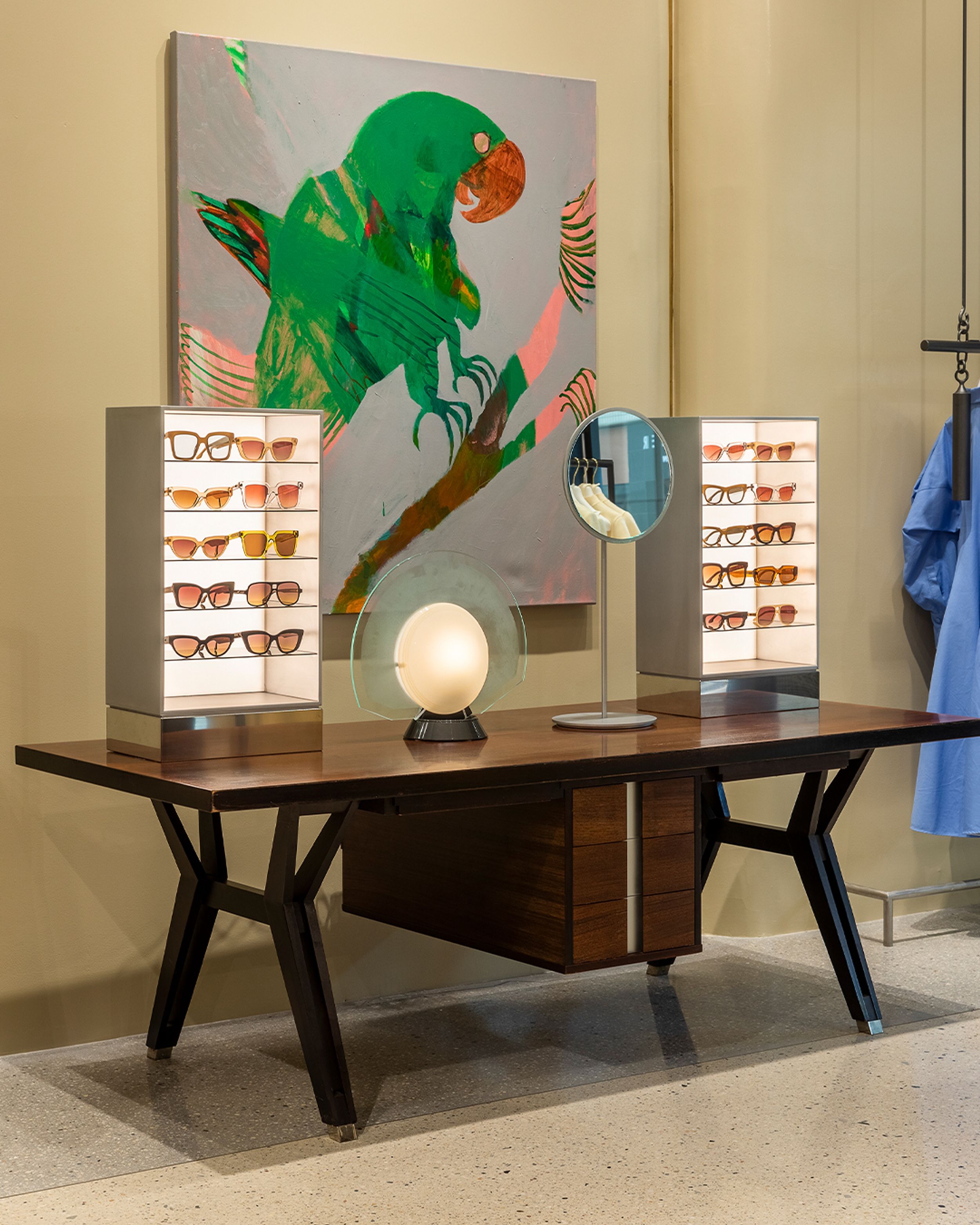 Interior of woman's fashion boutique featuring desk with a sunglasses display and large painting of a parrot on the wall