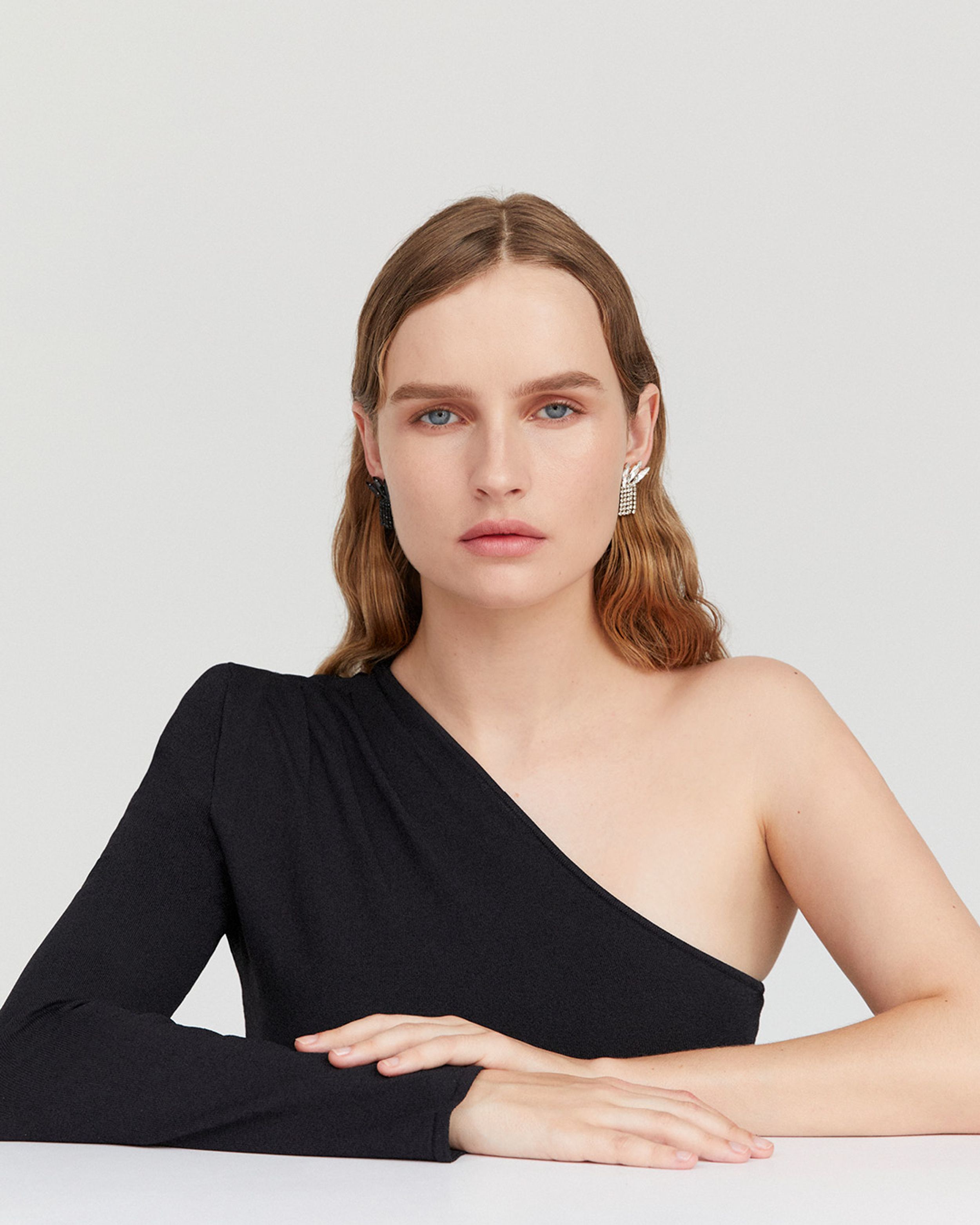 Olivia DeJonge gazing facing the camera wearing a black one-shouldered gown