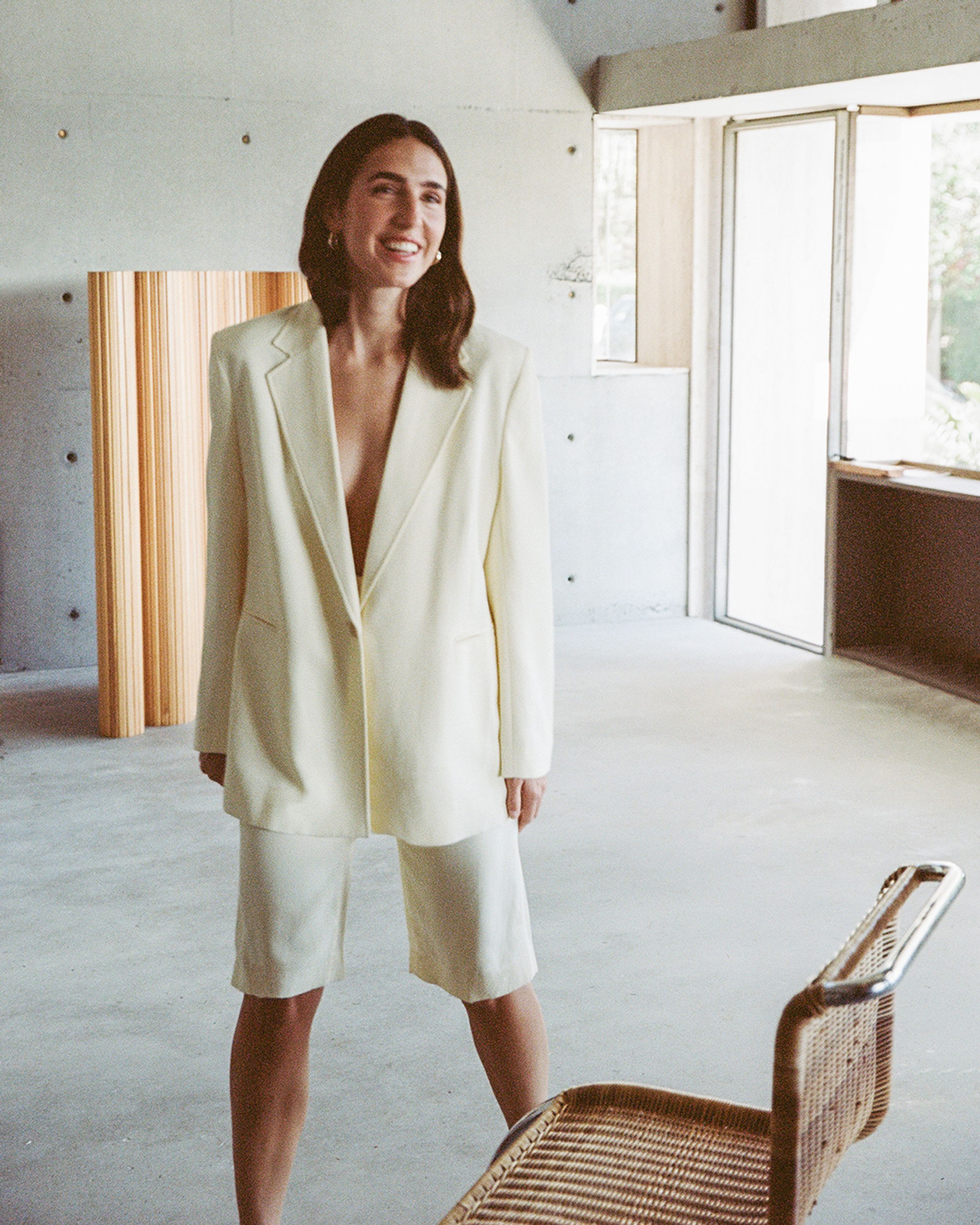 Bianca Marchi standing in a minimalistic living room wearing a cream oversized jacket and cream shorts