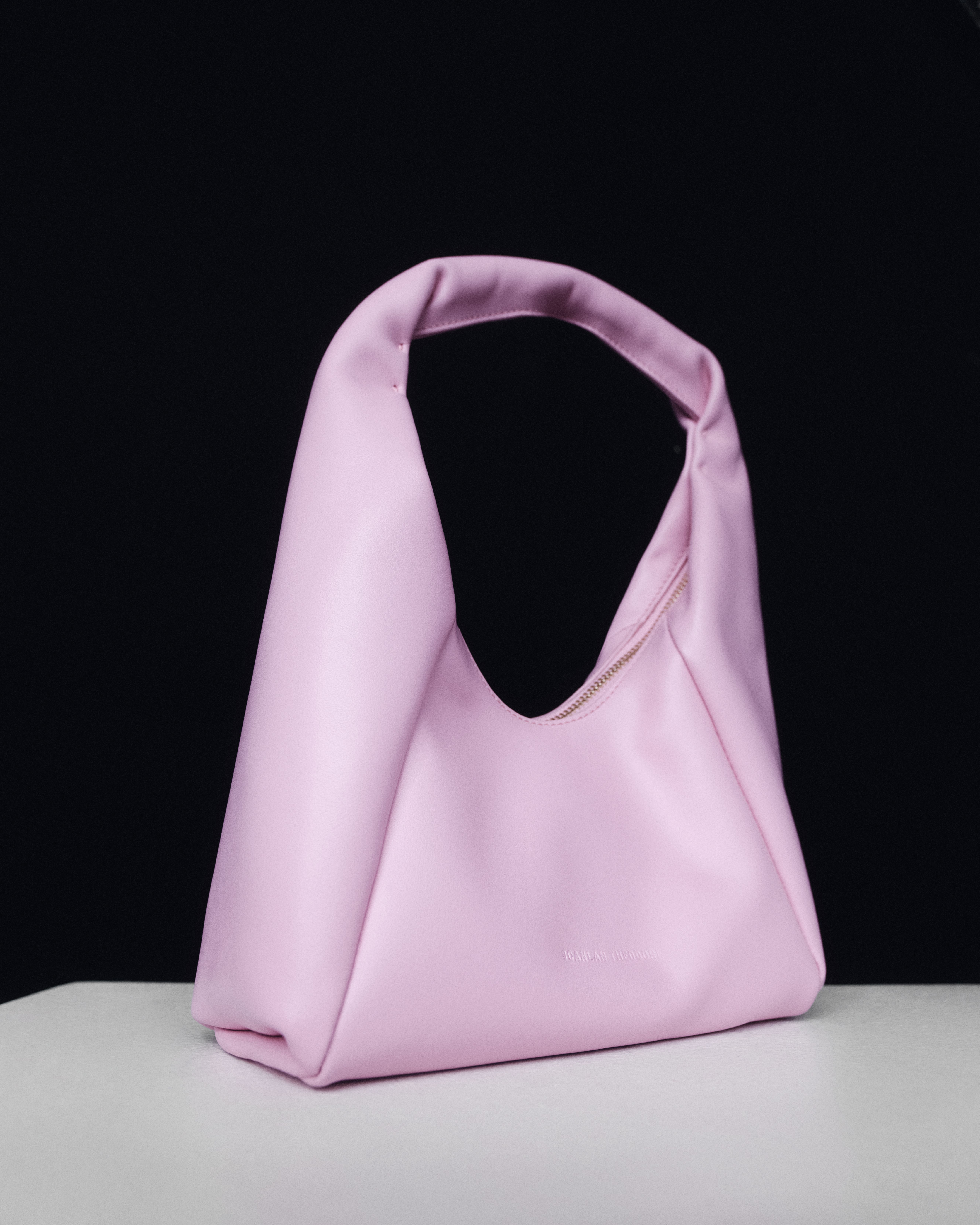 Light pink leather shoulder bag on a white surface with black wall