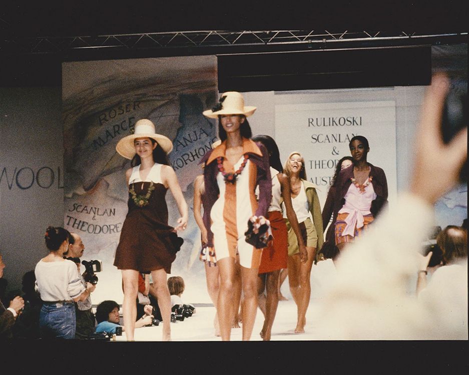 Seven models walking down the runway in a group smiling wearing summer clothing
