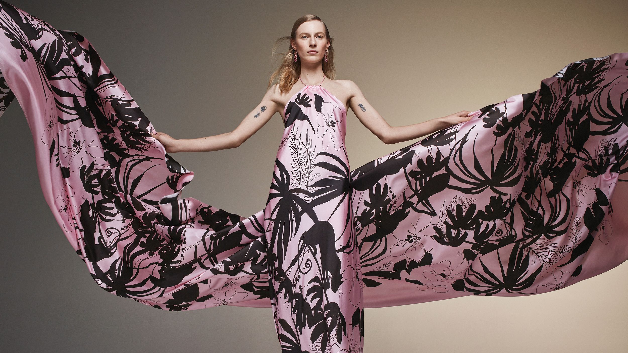 Julia Nobis wearing a long silk halterneck dress with black jungle print with arms outstretched