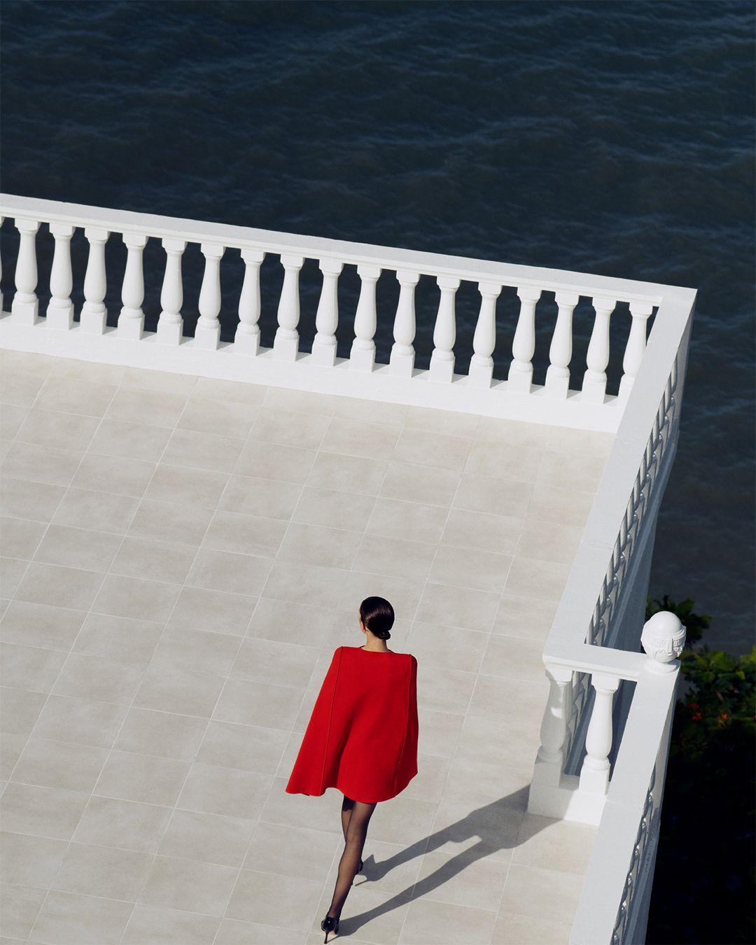 Aerial view of model in Crepe Knit Red Cape Dress walking toward balcony