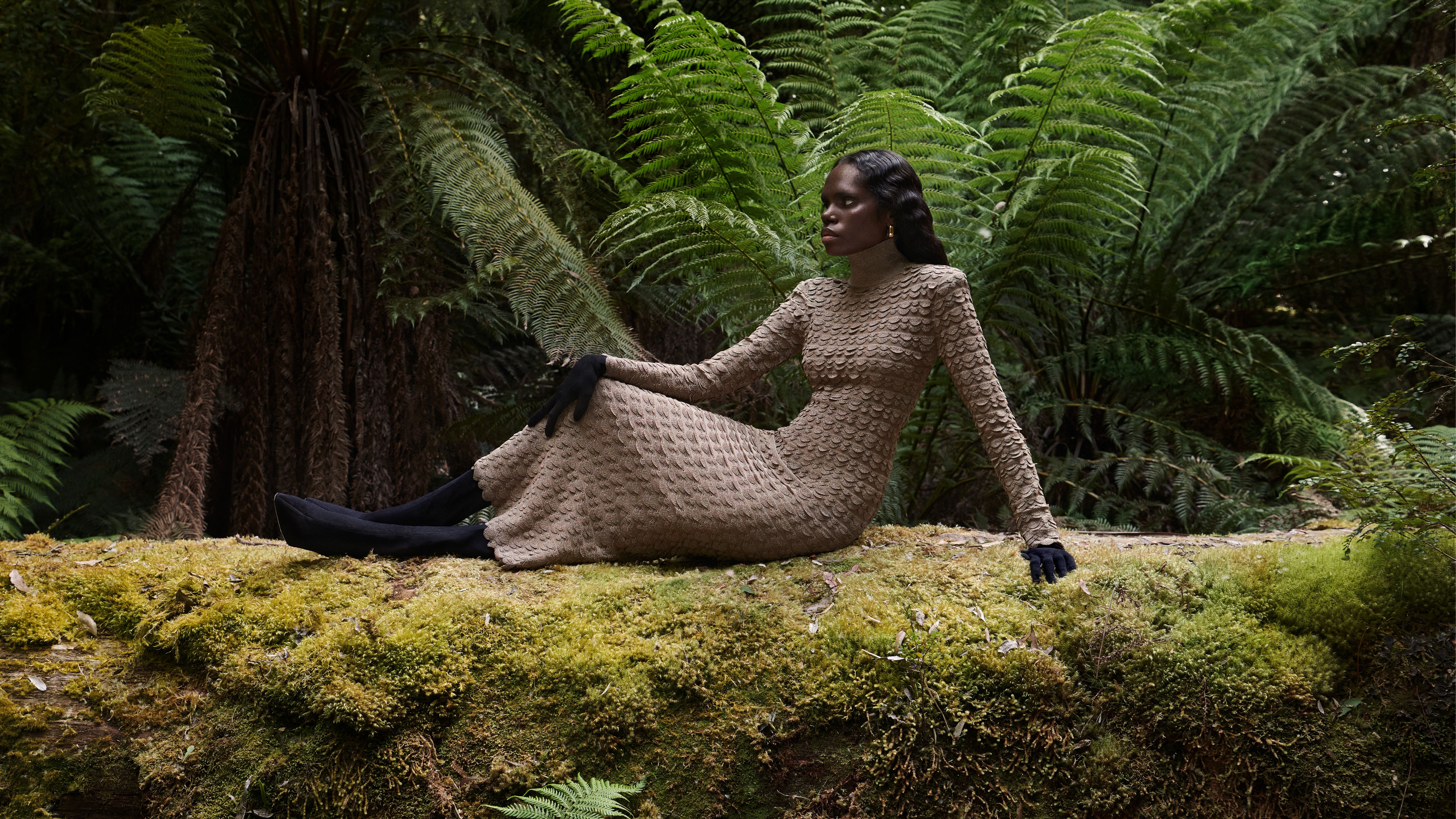 Tarlisa Gaykamangu reclined on moss in the forest wearing a brown knitted gown.