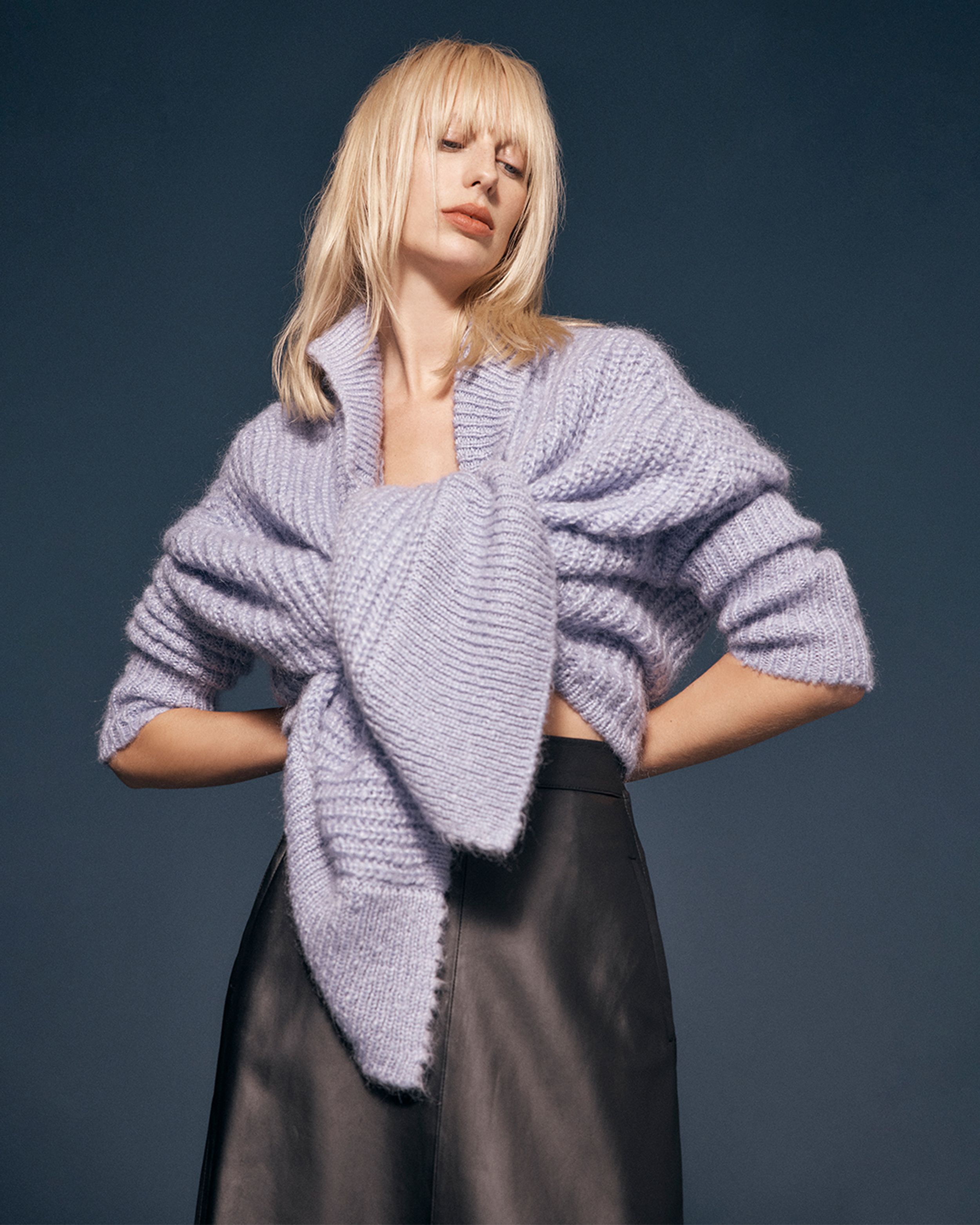Blonde model with hands on hips wearing a lilac chunky knit cardigan
