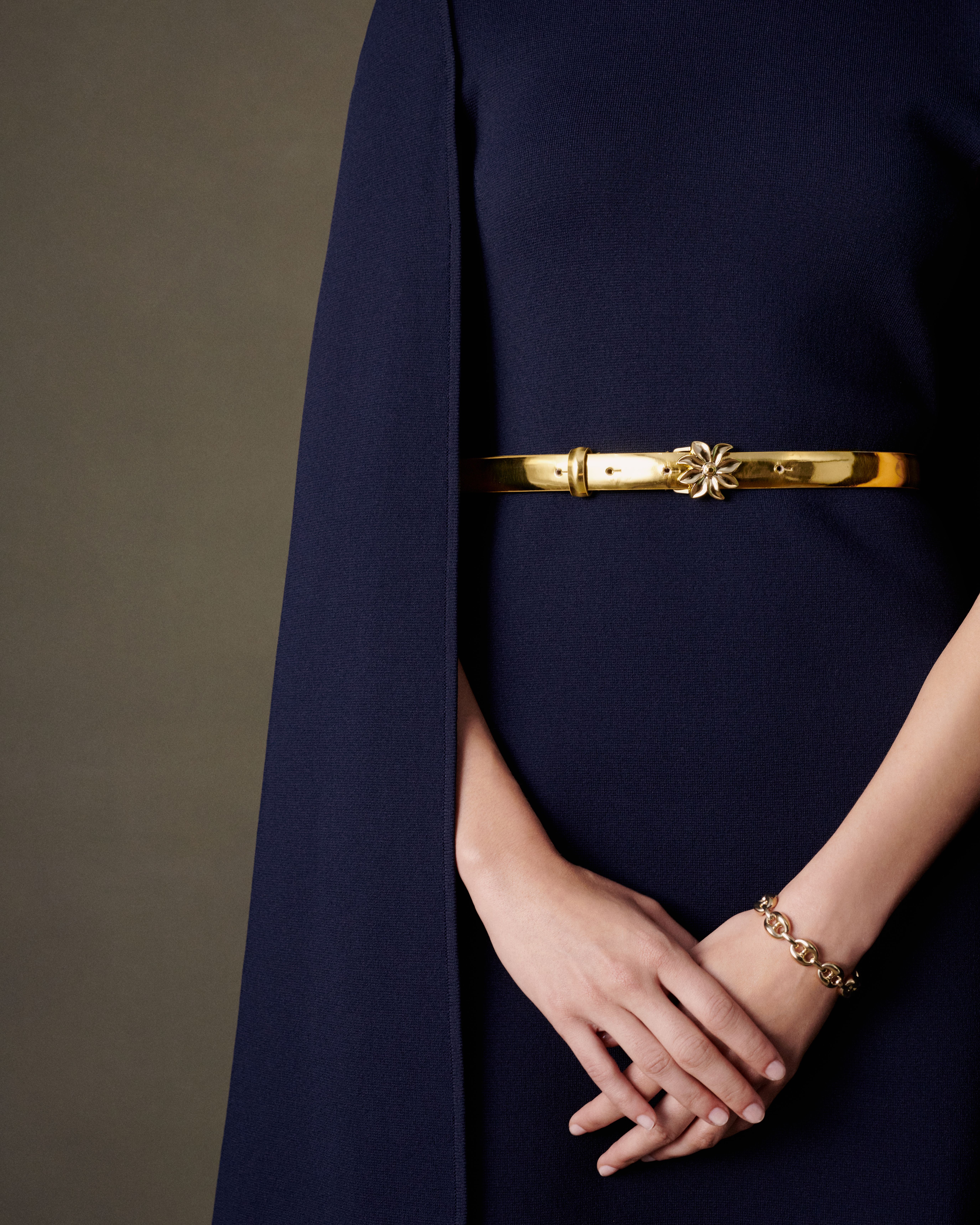 Close up of model wearing a navy Crepe Knit cape dress with a gold leather belt and gold chain bracelet